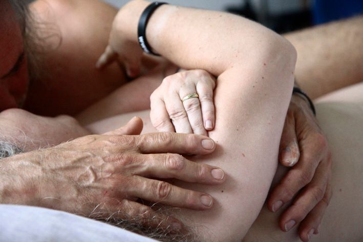 angedeutet: ein nacktes Paar im Bett  Man sieht nur einen Arm und die Hände der Frau und die kräftigen Hände des Mannes, der sie zärtlich berührt.