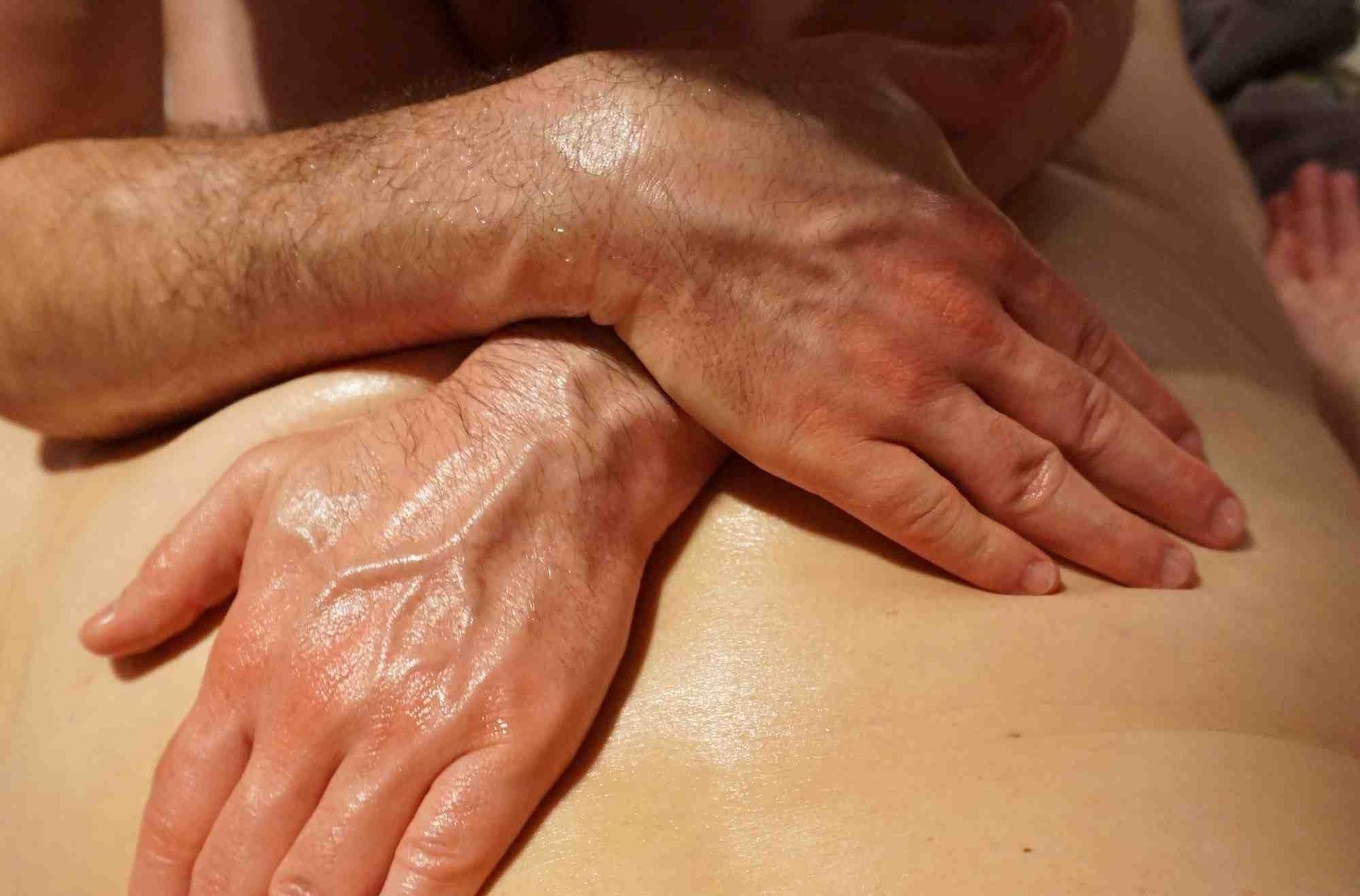 zwei ölglänzende Hände auf dem Rücken einer Person - als Symbol für liebevolle Berührung und tantrische Körperarbeit bei Tantra Massage und Sexualbegleitung