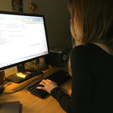 Eine Frau tippt in einem schwach beleuchteten Raum an einem Computer und konzentriert sich auf den Bildschirm.