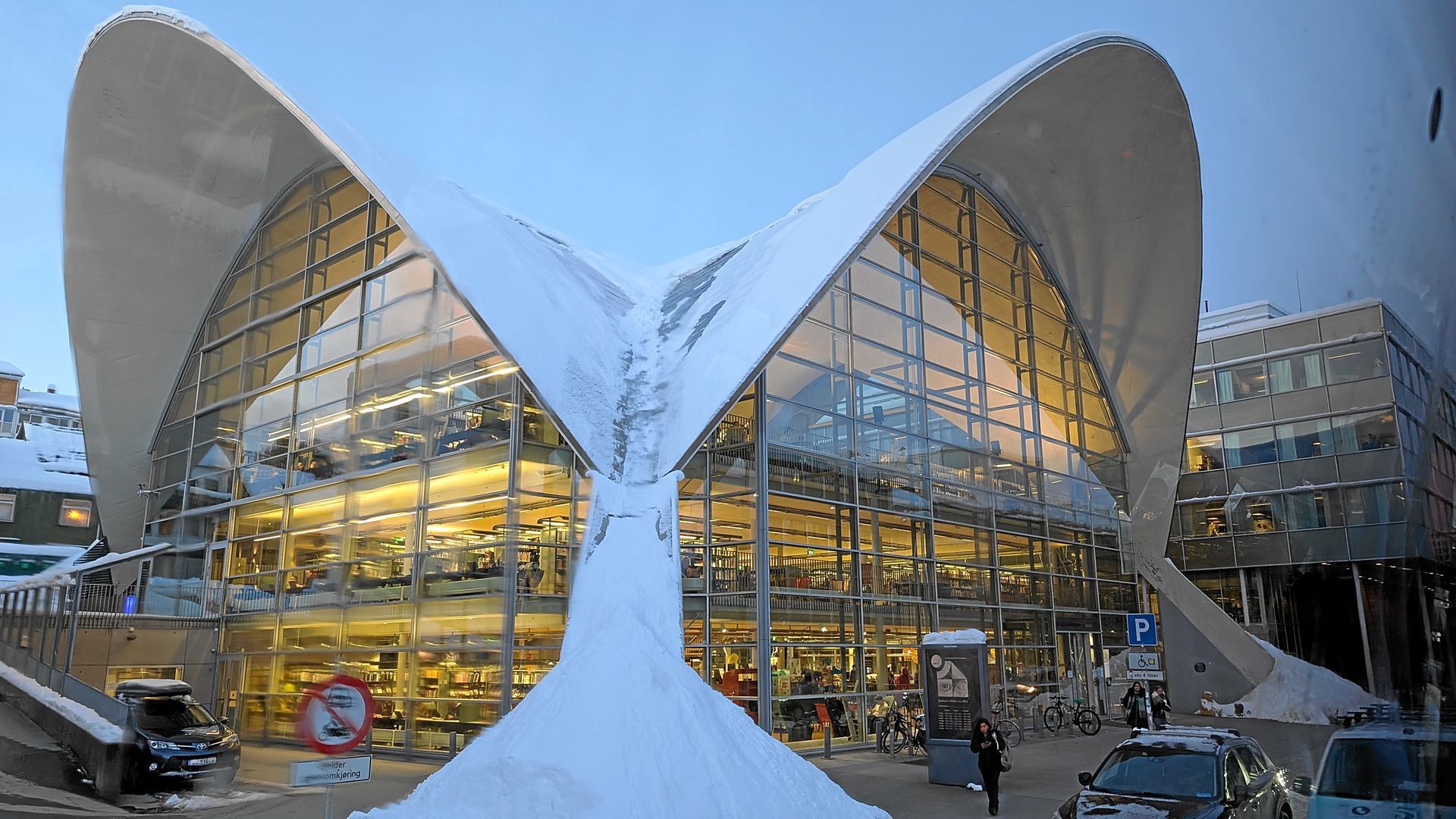 Modernes Gebäude mit geschwungenem weißen Dach, schneebedeckter Fassade und großen Glasfenstern, Tromsø, Norwegen.
