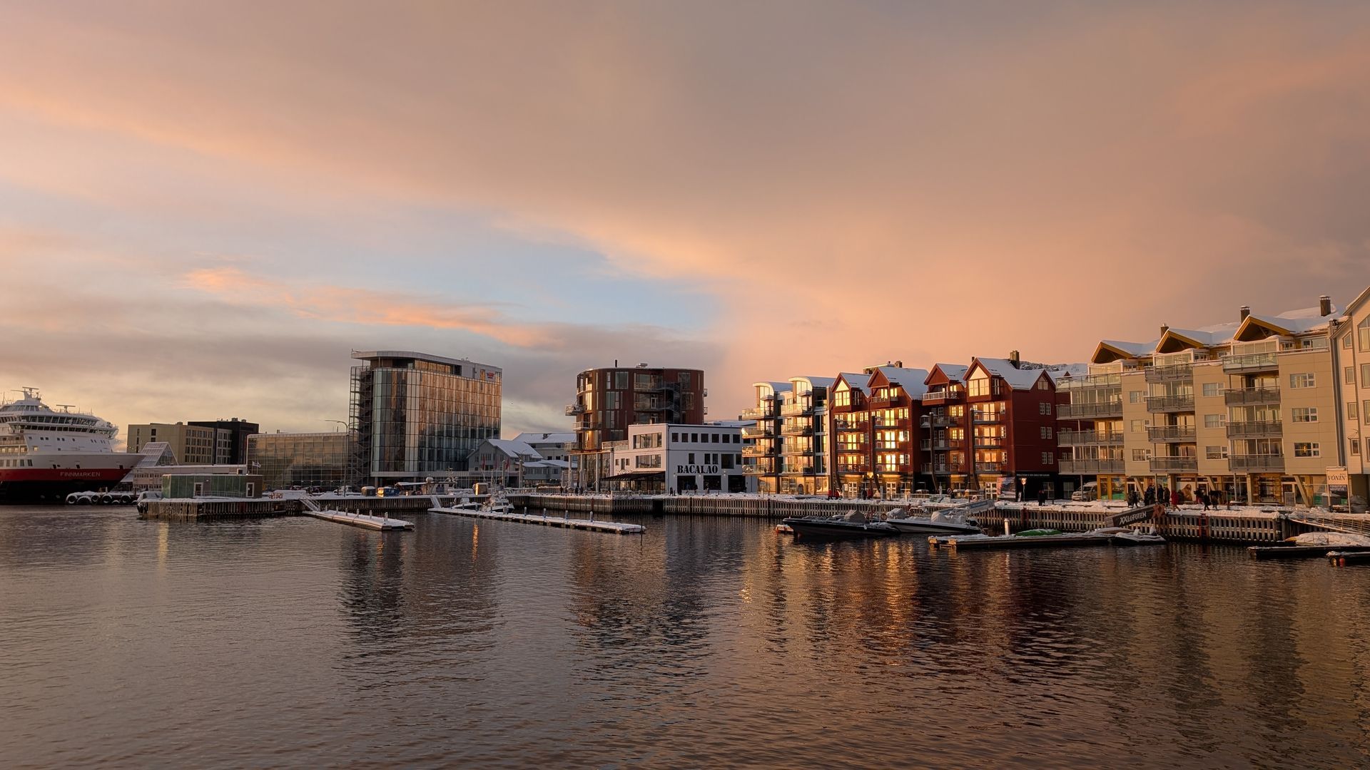 Hafenblick bei Sonnenuntergang, Gebäude mit schneebedeckten Dächern, die sich im Wasser spiegeln.