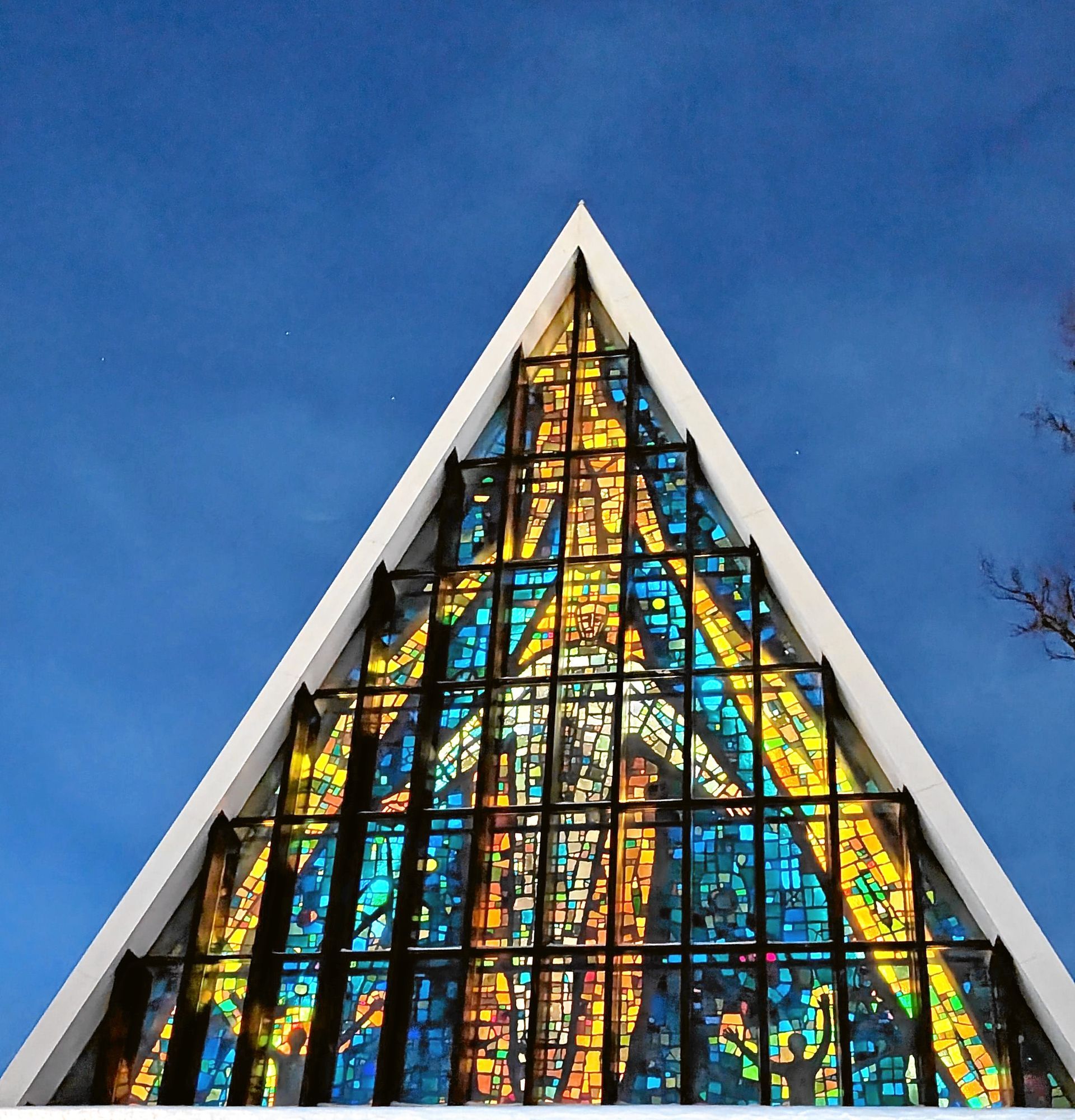 Dreieckige Kirchenfassade mit Buntglasfenstern vor blauem Himmel.