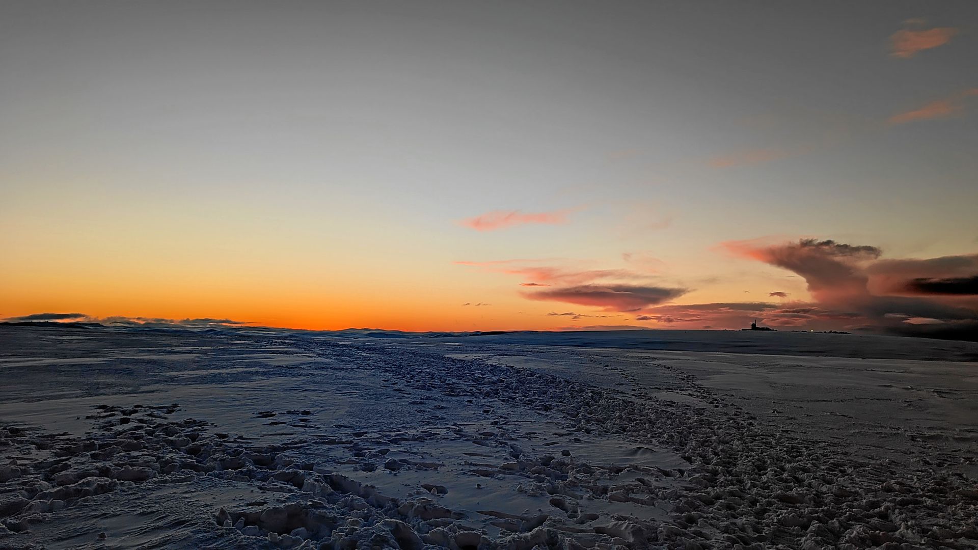 Schneebedeckte Landschaft mit einem leuchtend orange-rosa Sonnenuntergang im Hintergrund.