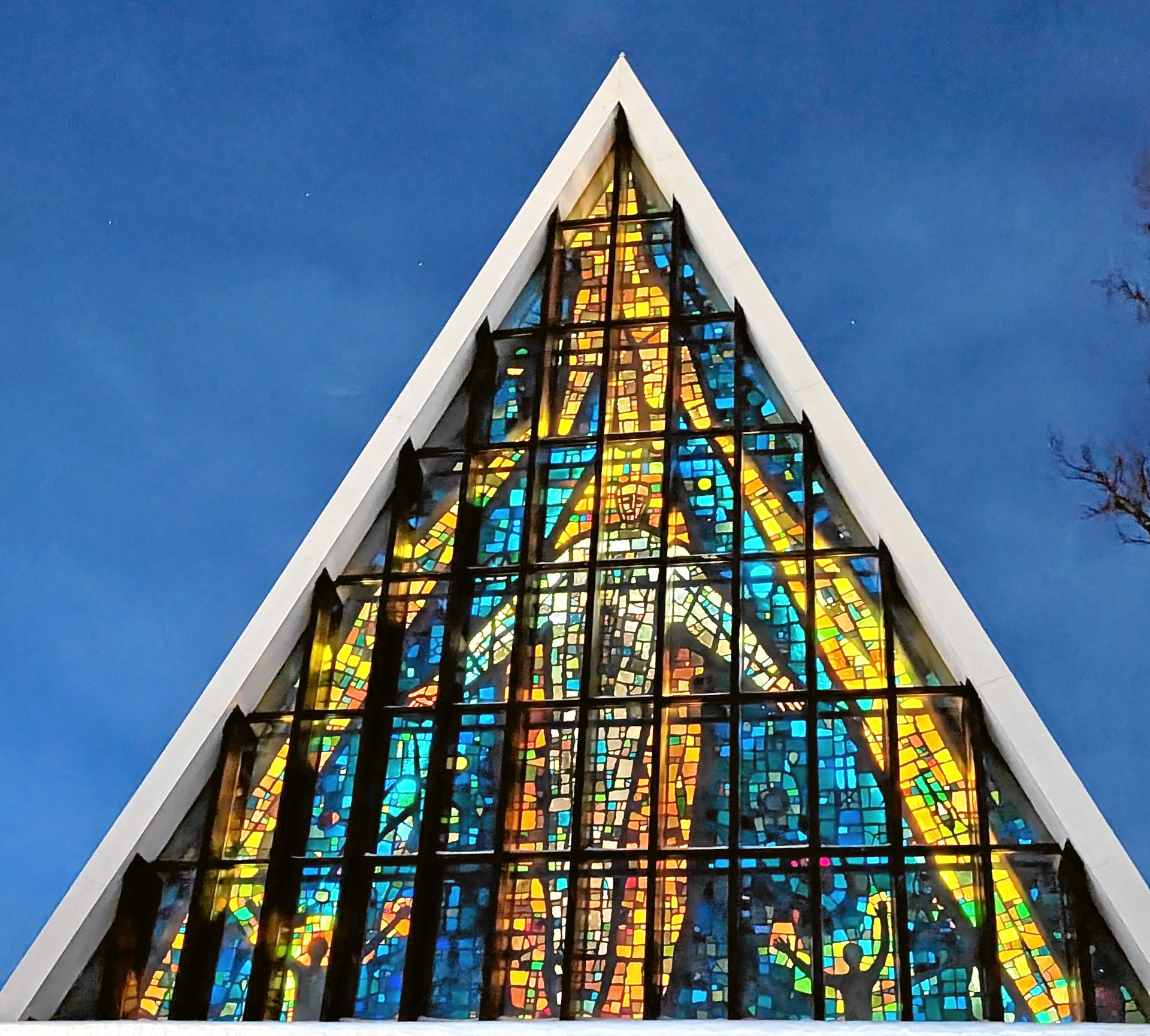 Dreieckige Kathedralenfassade mit großem, farbenprächtigem Buntglasfenster vor blauem Himmel.