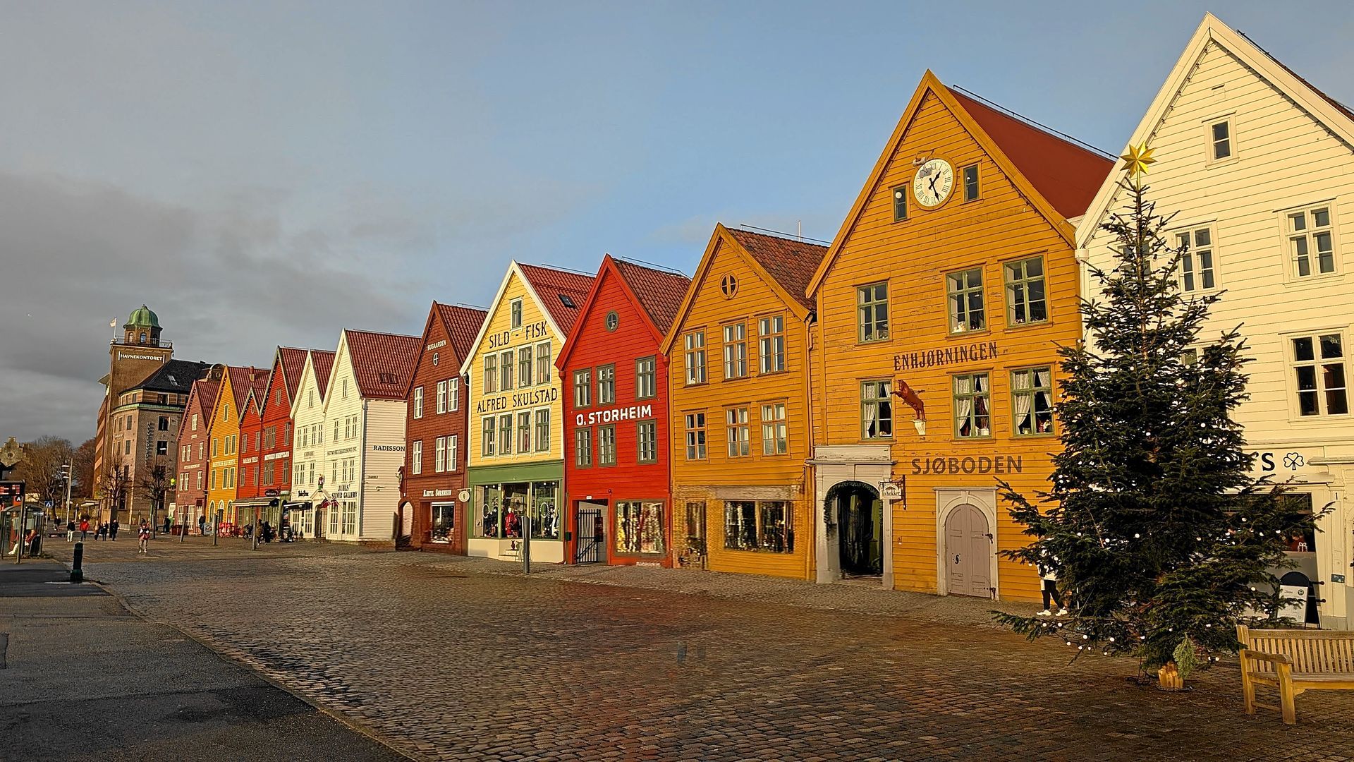 Bunte Holzhäuser mit Giebeldächern säumen eine Kopfsteinpflasterstraße in Bergen, Norwegen.