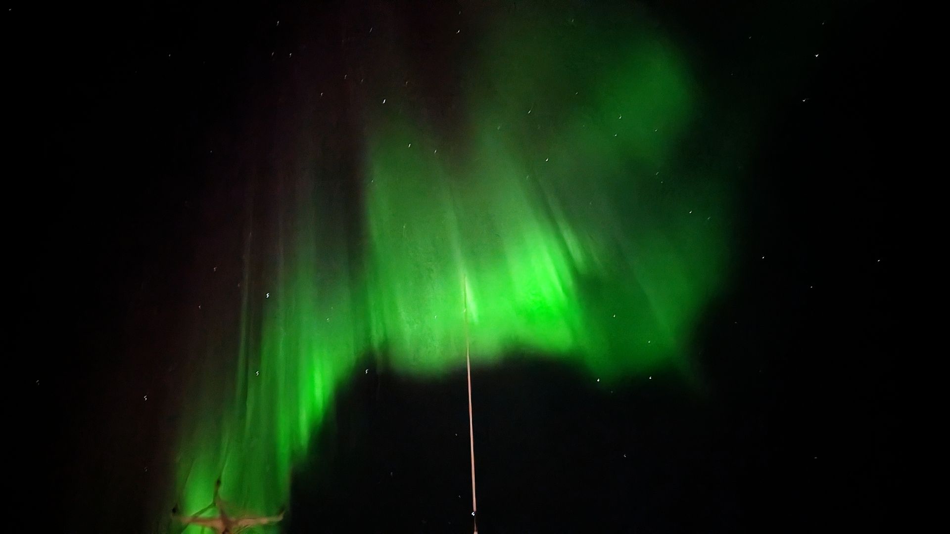 Grüne Nordlichter vor schwarzem Himmel; eine schwache, dünne Linie ist sichtbar.