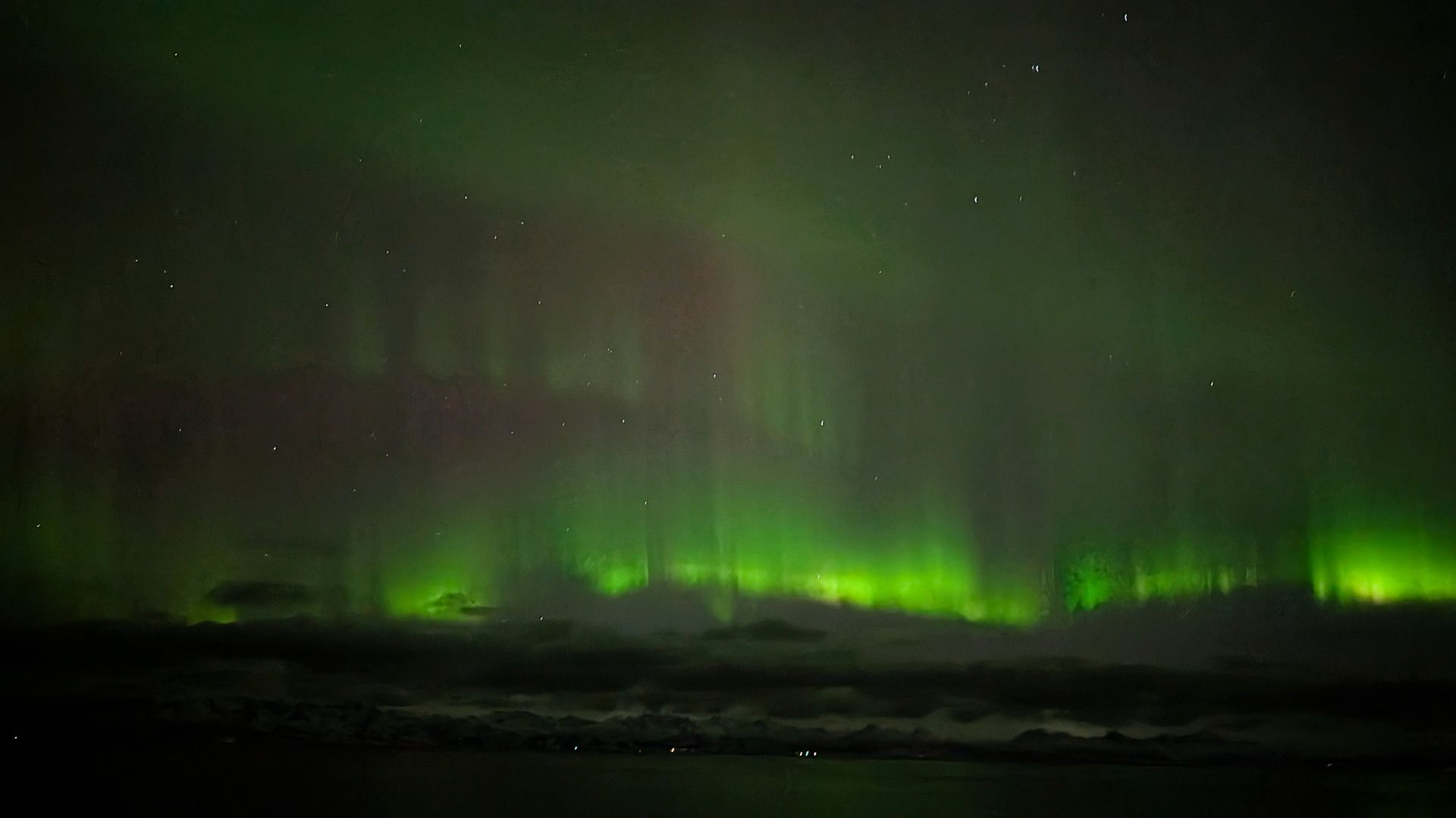 Grüne Nordlichter über dunklem, silhouettenhaftem Land oder Meer.
