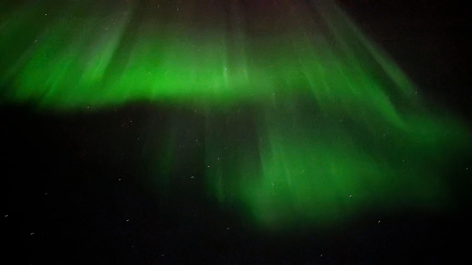 Grüne Nordlichter tanzen über einen dunklen Nachthimmel mit sichtbaren Sternen.