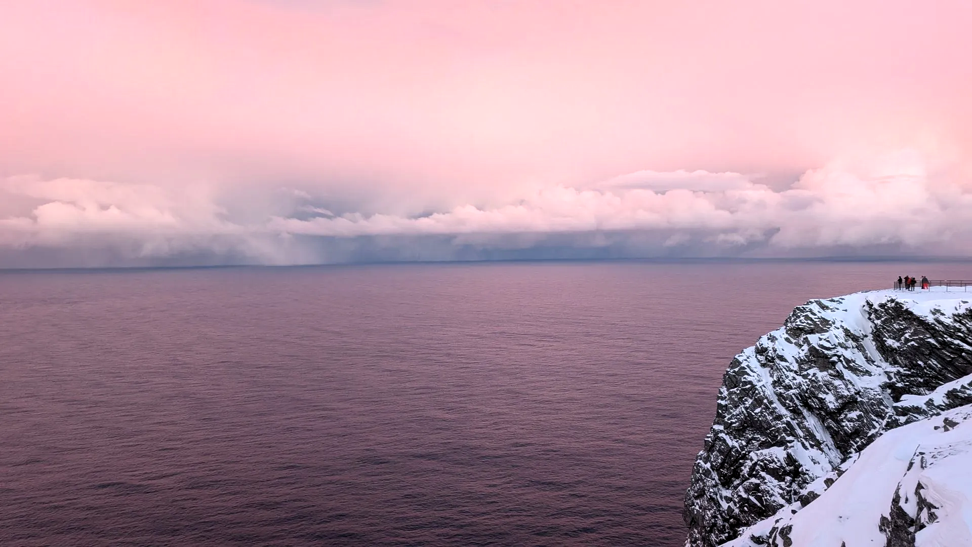 Rosa Himmel über ruhigem Meer, rechts schneebedeckter Klippenrand mit einigen Gestalten.