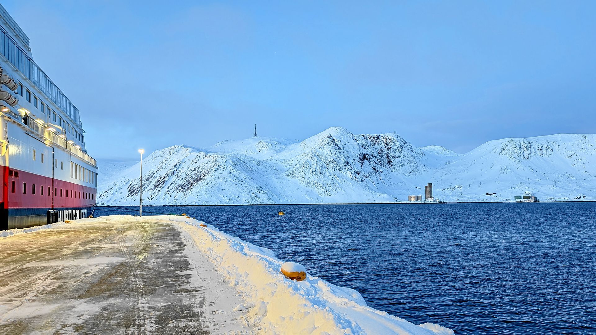 Ein Kreuzfahrtschiff liegt im verschneiten Hafen vor Anker, im Hintergrund erheben sich die Berge.