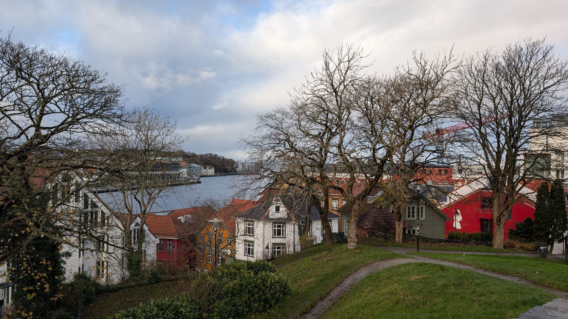 Häuser mit rot-weißen Fassaden säumen einen Hügelhang und überblicken ein Gewässer unter einem bewölkten Himmel.