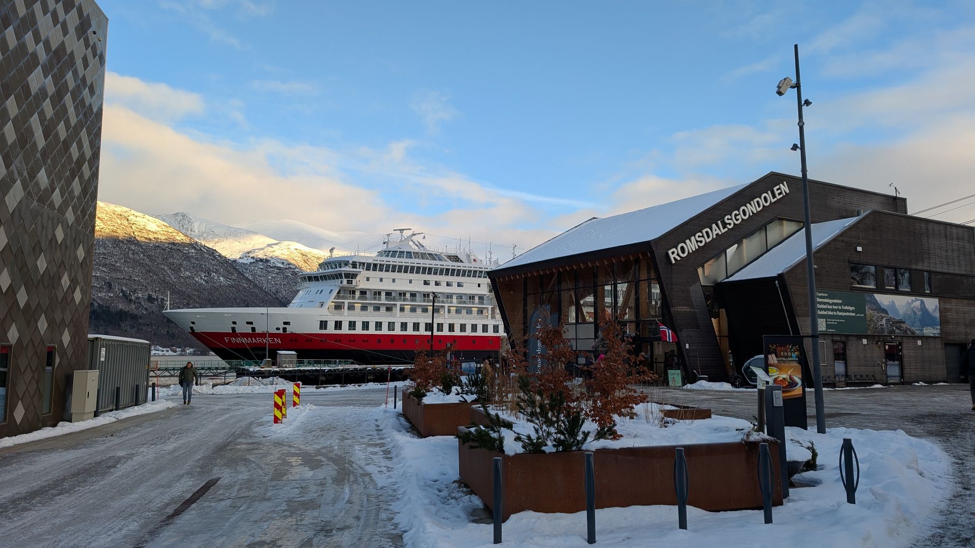 Ein großes rot-weißes Kreuzfahrtschiff lag in der Nähe eines schneebedeckten Gebäudes in einem Hafen vor rAnker.