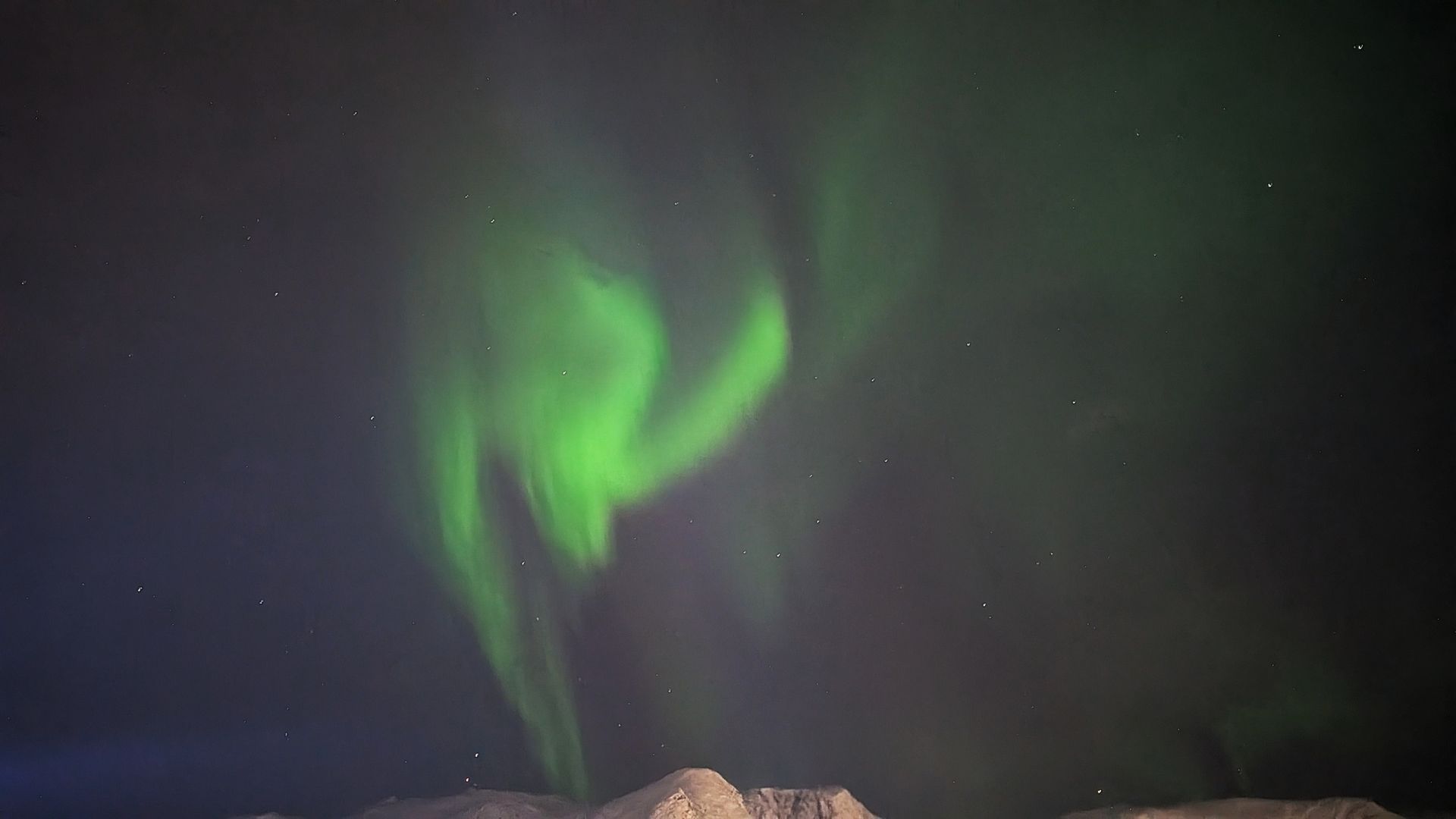 Grüne Nordlichter wirbeln am dunklen Nachthimmel über einer schneebedeckten Landschaft.