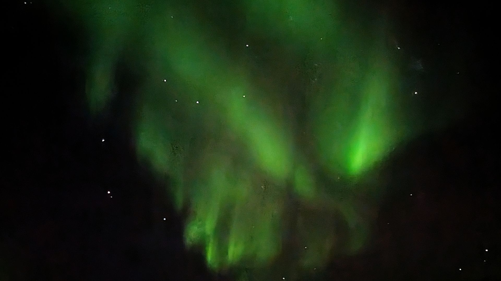 Grüne Nordlichter wirbeln über den dunklen Nachthimmel; im Hintergrund sind Sterne zu sehen.