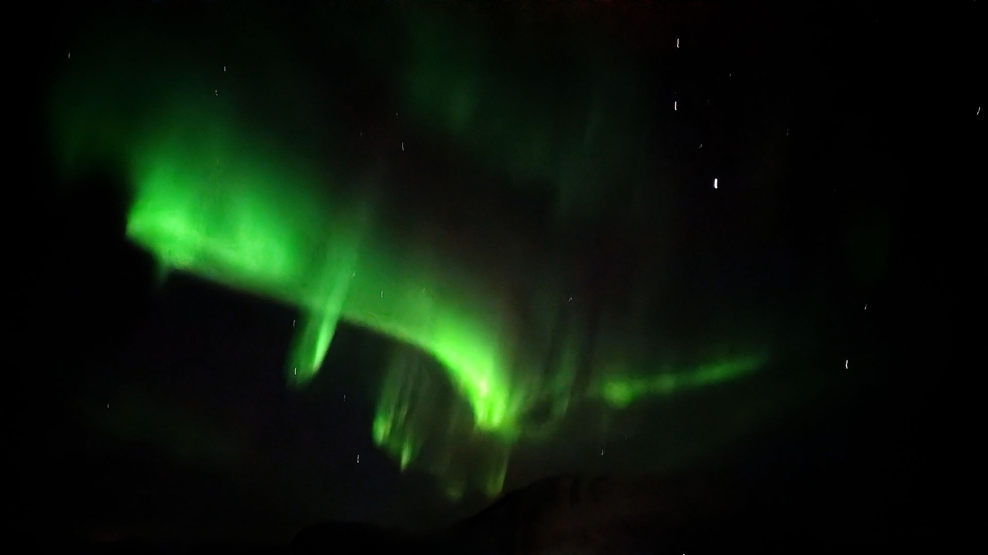 Grüne Nordlichter tanzen über einen dunklen Nachthimmel mit sichtbaren Sternen.