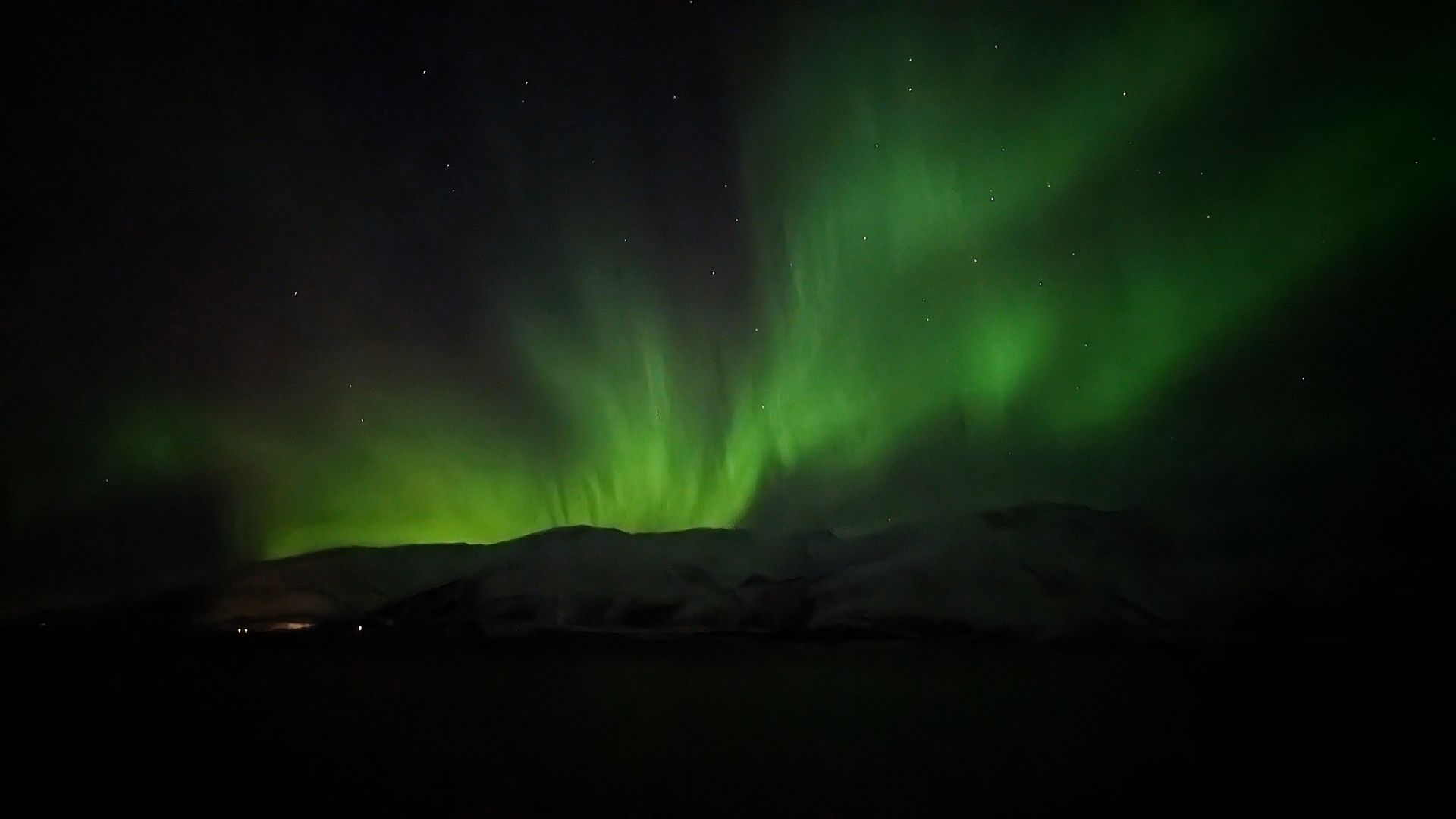 Grüne Nordlichter tanzen über schneebedeckten Bergen vor einem sternenklaren Nachthimmel.
