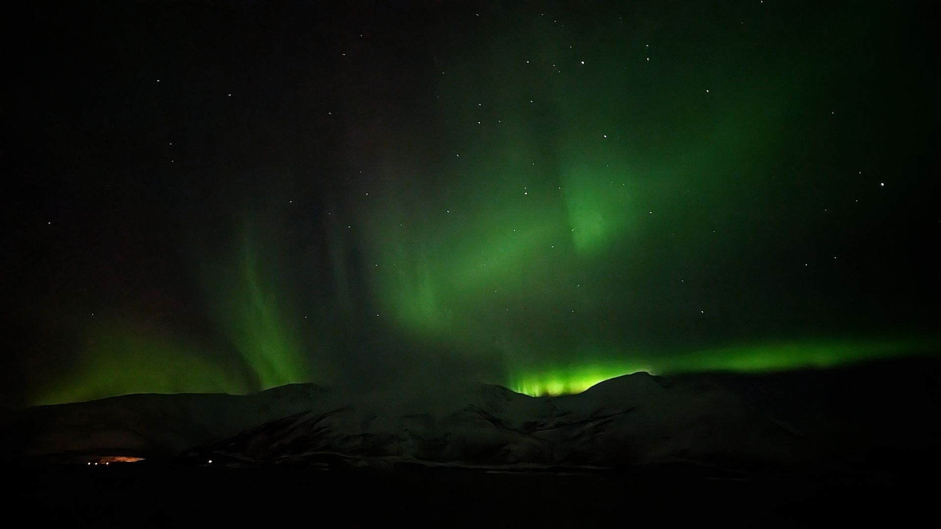 Grüne Nordlichter über dunklen Bergen und sternenklarem Himmel.