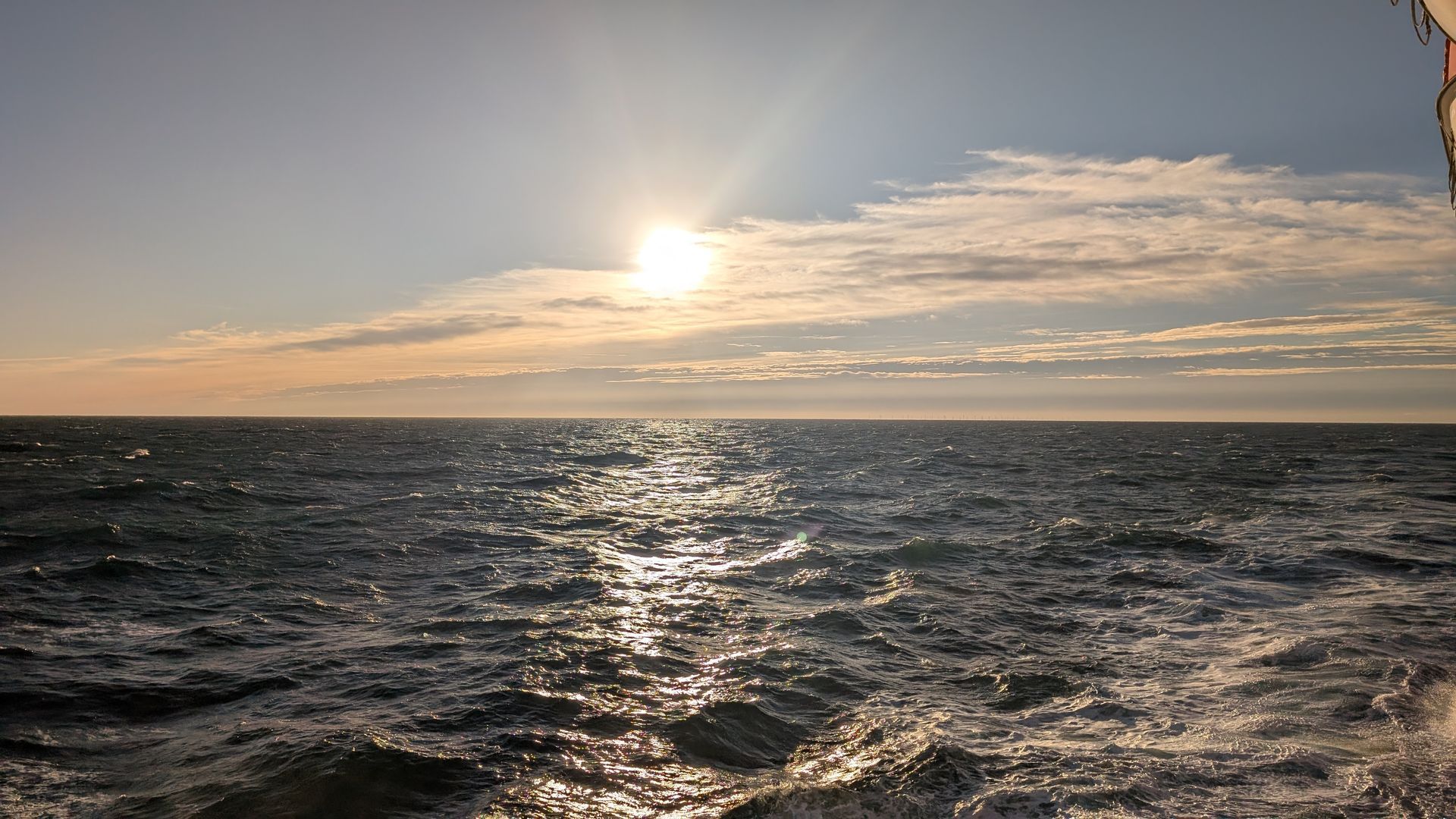 Die Sonne scheint über einen welligen Meereshorizont mit Wolken.