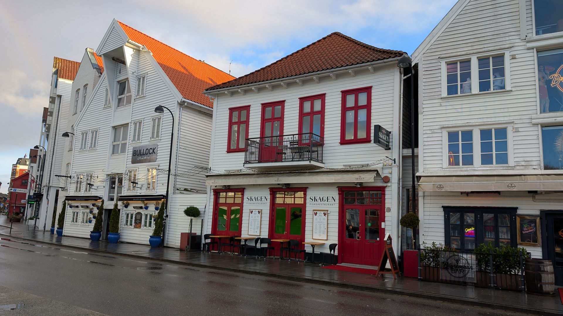 Eine Reihe weißer Gebäude mit roten Türen und Fenstern an einer nassen Straße.