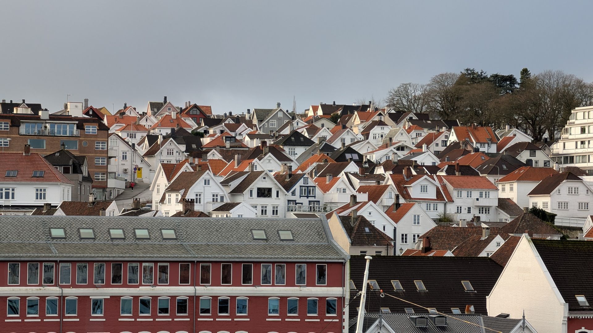Weiße Häuser mit roten Ziegeldächern schmiegen sich unter einem bewölkten Himmel an einen Hang.