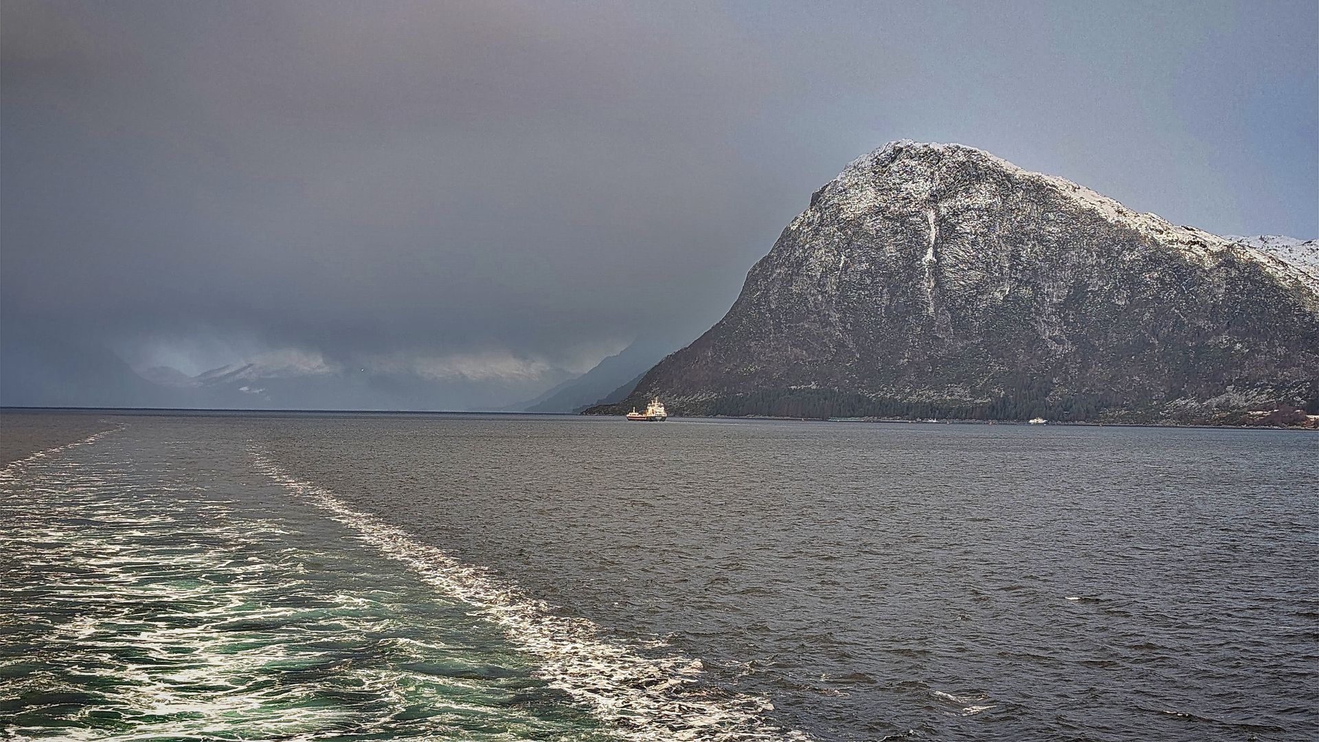 Dunkles, aufgewühltes Meer mit einem schneebedeckten Berg unter einem bewölkten Himmel.