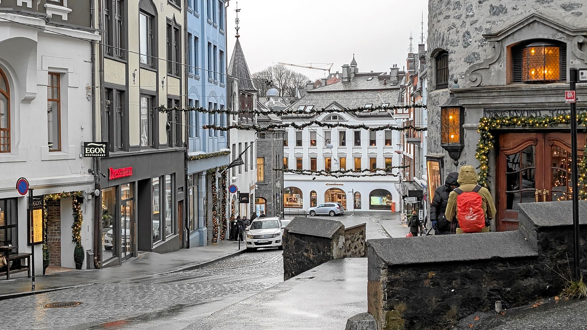 Steinstraße in einer europäischen Stadt, Gebäude auf beiden Seiten, Weihnachtsdekorationen, Person mit rotem Rucksack.