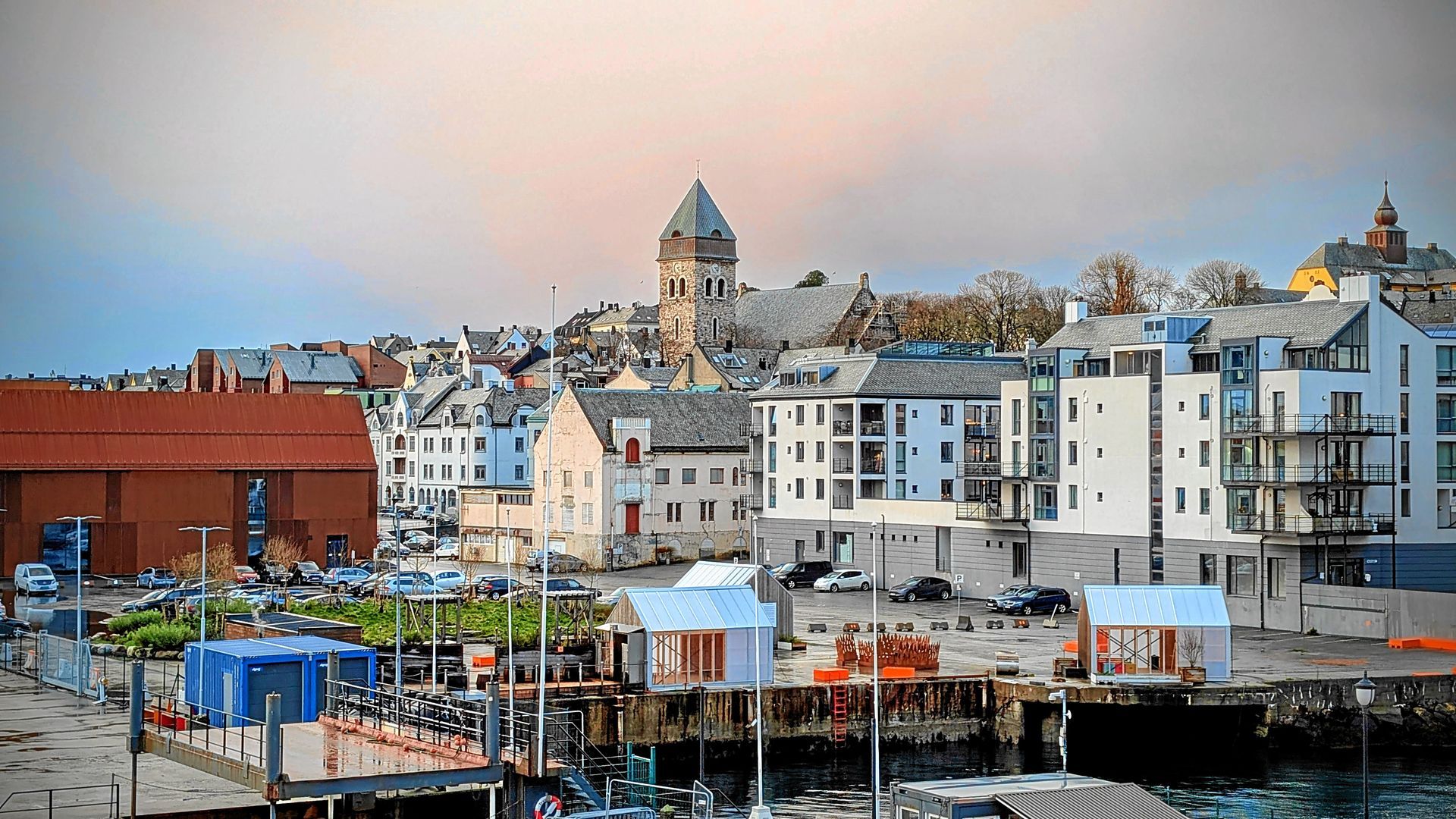 Küstenstadt mit Gebäuden und Kirchturm, gesehen von einem Hafen mit Baustelle.