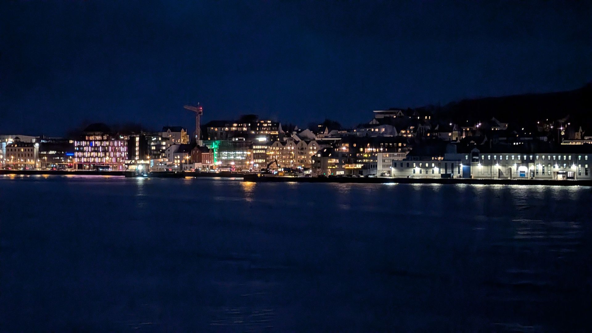 Nachtansicht einer Stadtsilhouette, deren helle Lichter sich im dunklen Wasser spiegeln.