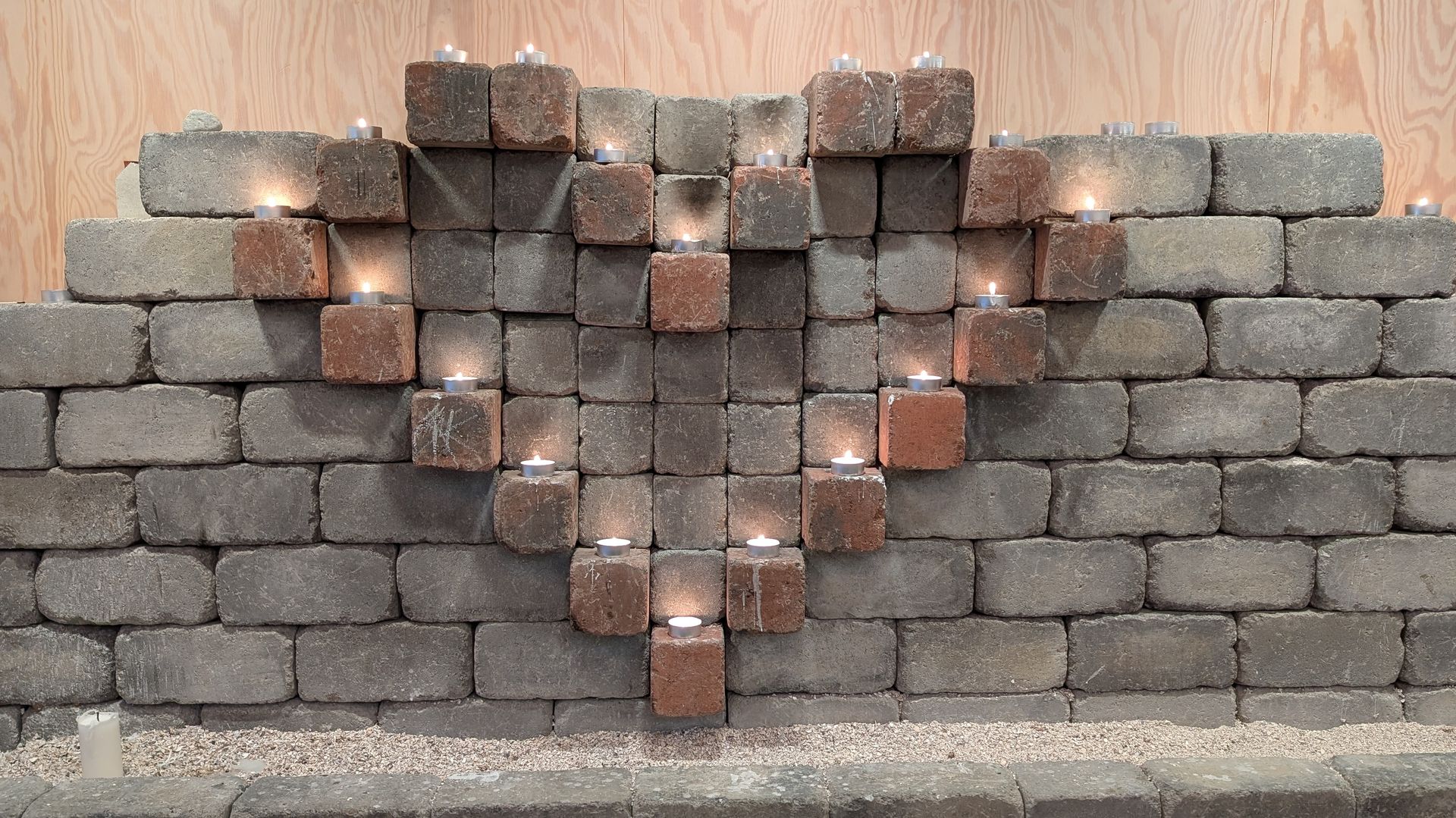Herzförmiges Gebilde aus Ziegelsteinen mit brennenden Kerzen.