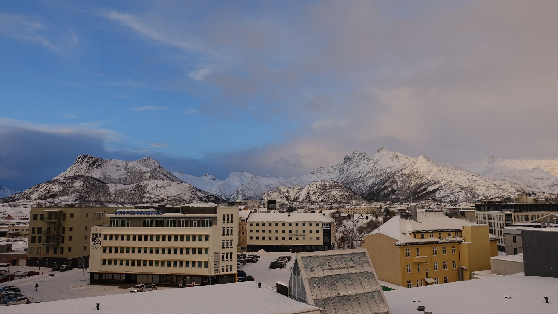 Schneebedeckte Gebäude in einer Stadt vor dem Hintergrund der Berge unter einem blauen und bewölkten Himmel.