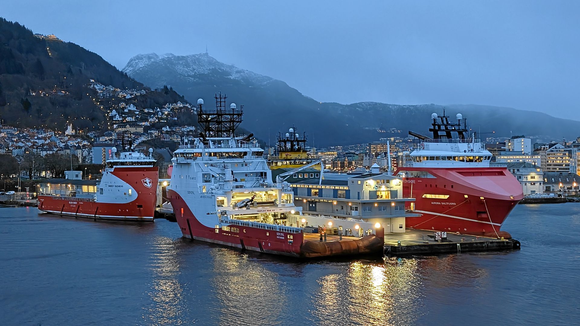 Drei rot-weiße Offshore-Versorgungsschiffe liegen in der Abenddämmerung in einem Hafen vor Anker.