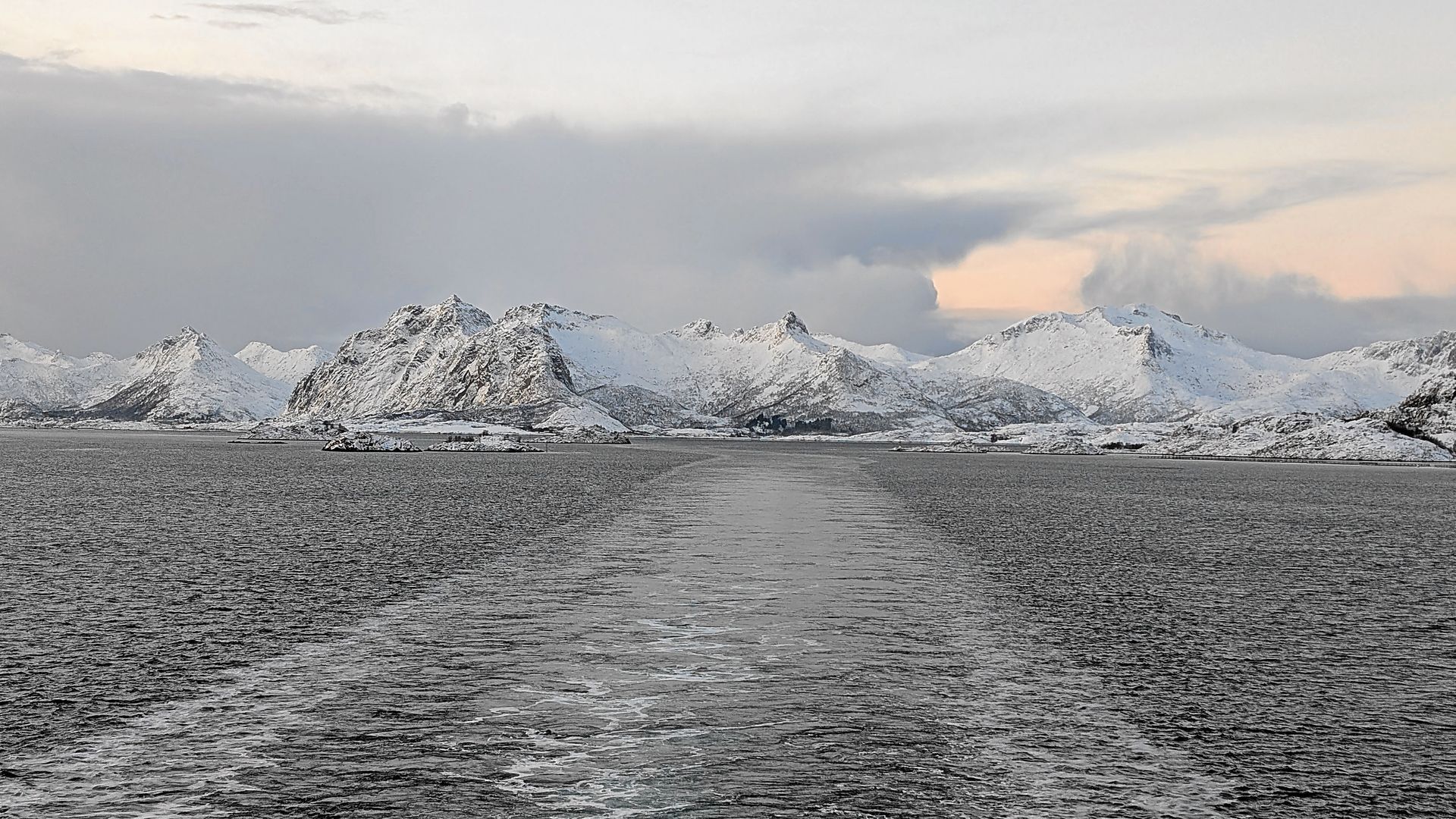 Verschneite Berge über einem Gewässer unter bewölktem Himmel.