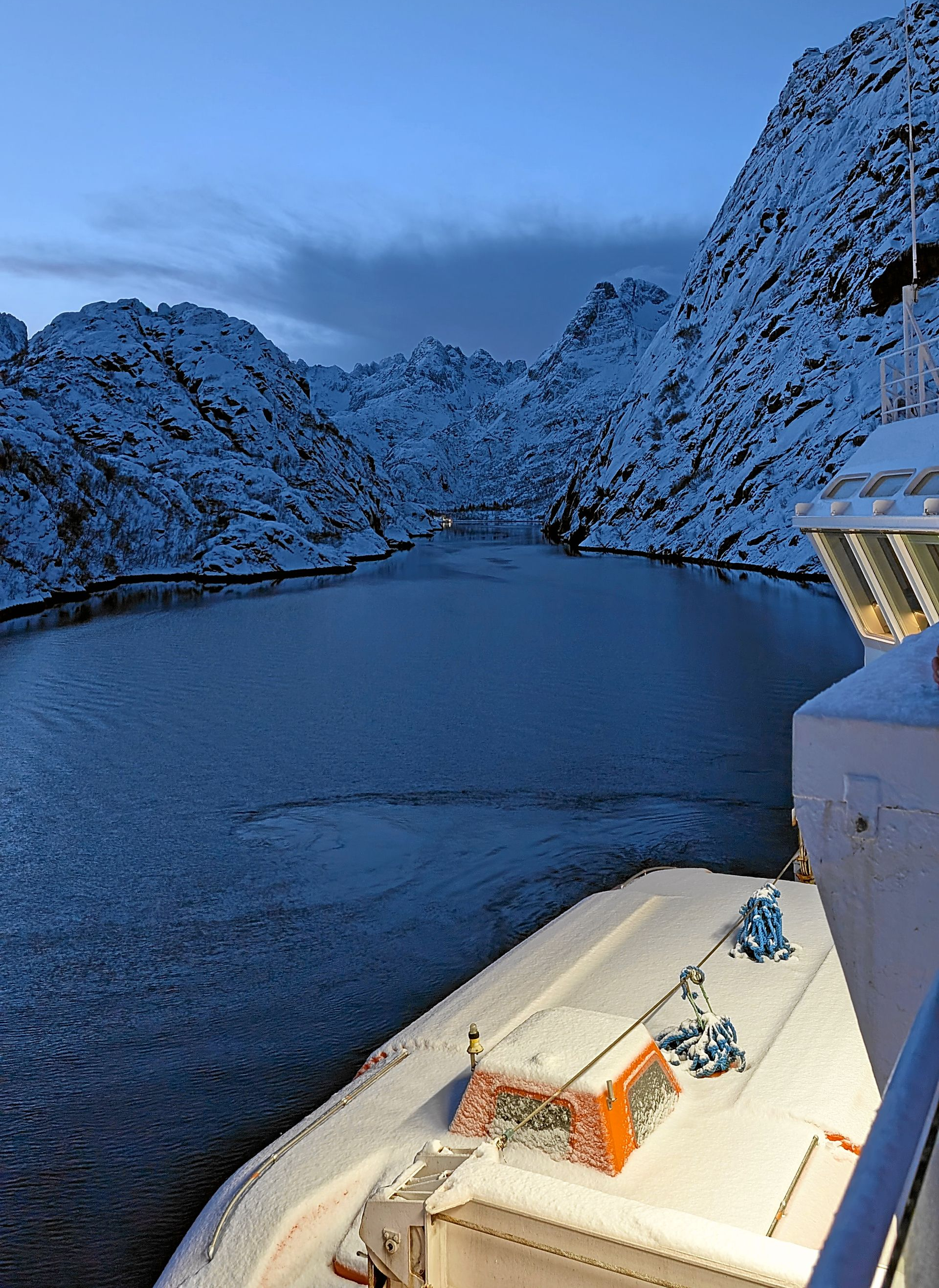 Vom Deck eines Schiffes aus gesehen, säumen schneebedeckte Berge einen dunklen Fjord.