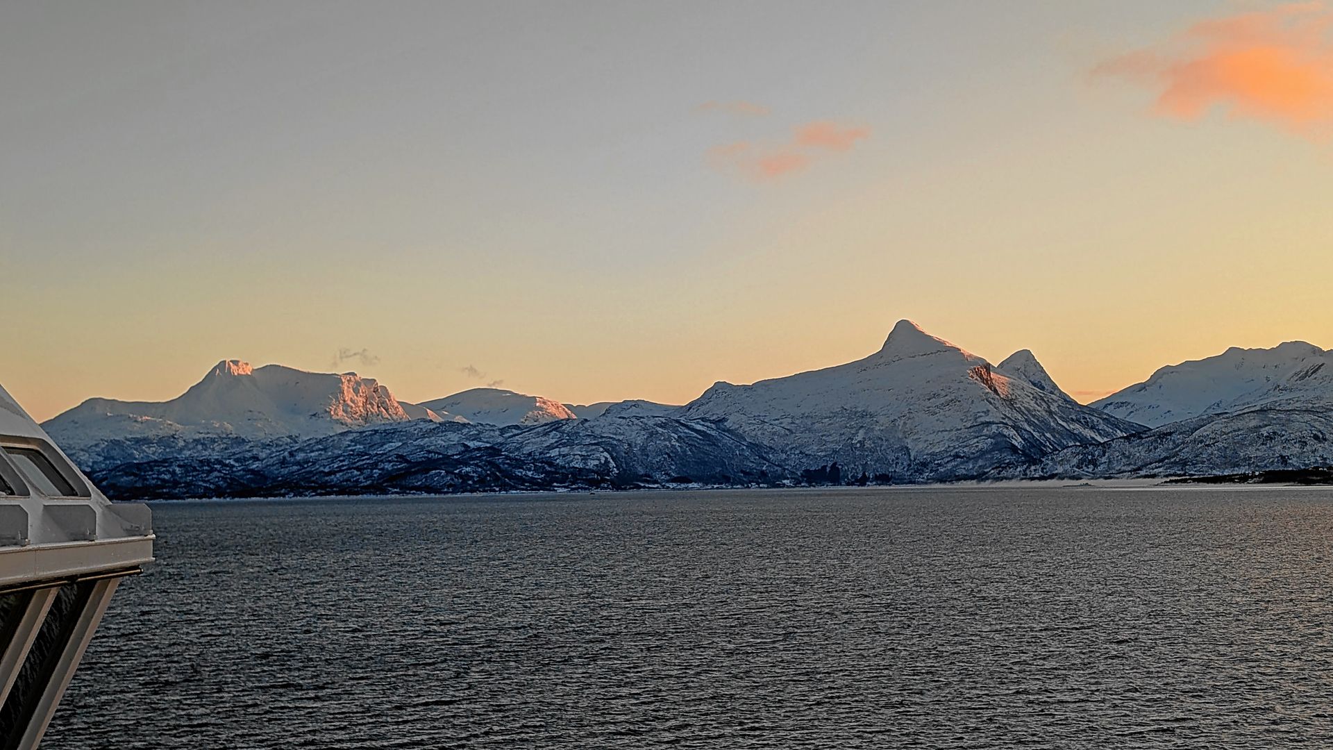 Schneebedeckte Berge im Sonnenuntergang über einem Gewässer. Oranger und rosafarbener Himmel.