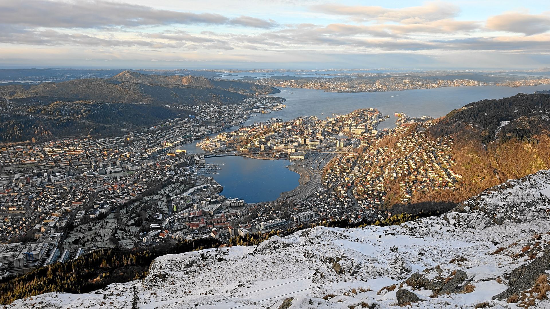 Stadtbild mit einem Gewässer, schneebedeckten Bergen und einem bewölkten Himmel.