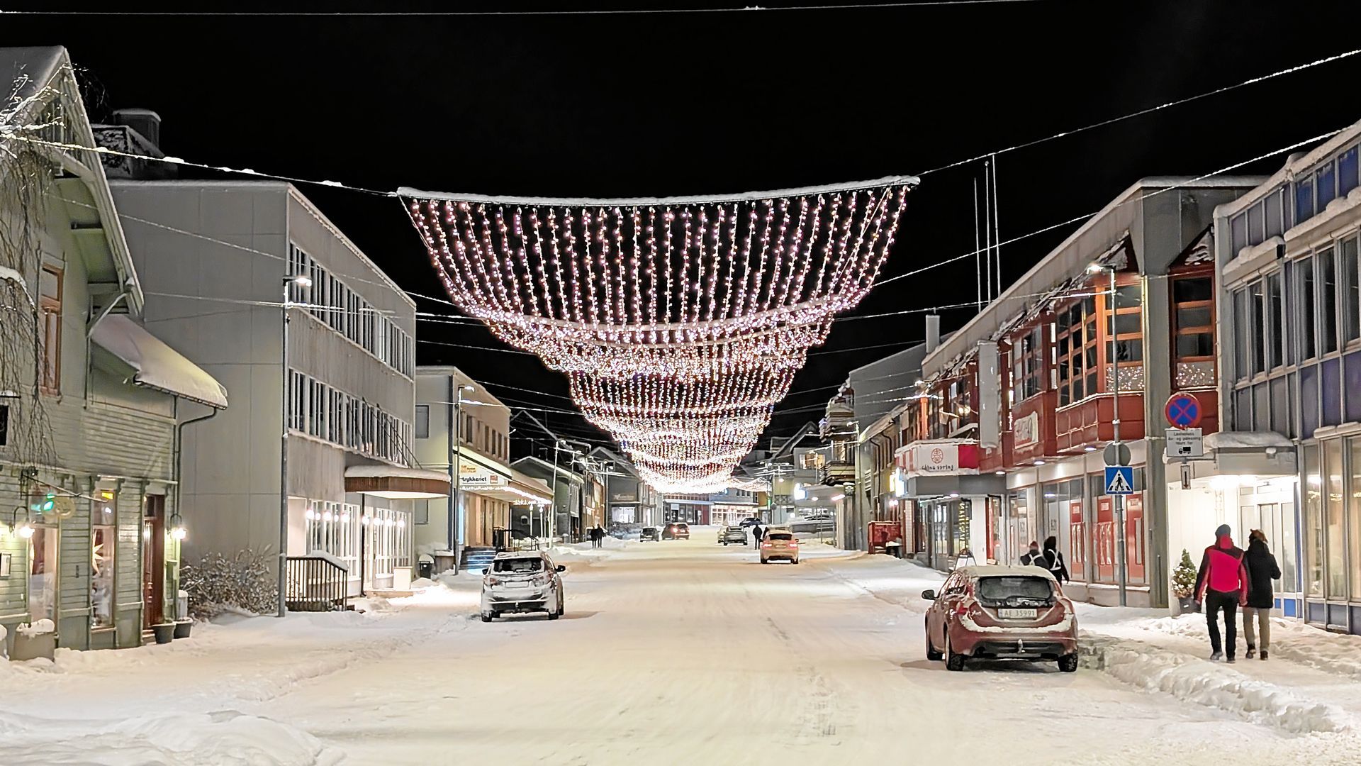 Verschneite Straße bei Nacht, über der festliche Lichterketten hängen.