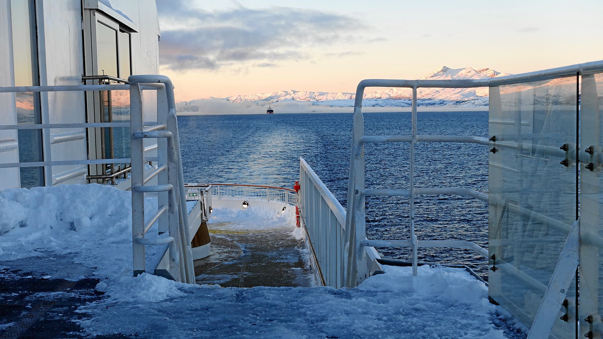 Verschneites Schiffsdeck mit Blick auf den eisigen Ozean und die Berge bei Sonnenuntergang.