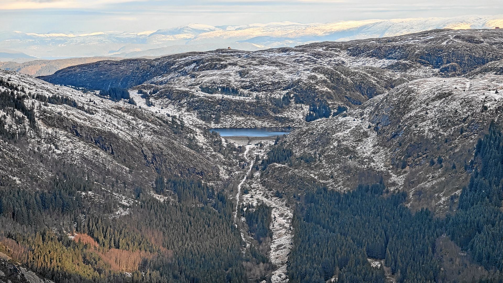 Eine schneebedeckte Bergkette mit einem See in ihrer Mitte. Immergrüne Bäume bedecken die Hänge.