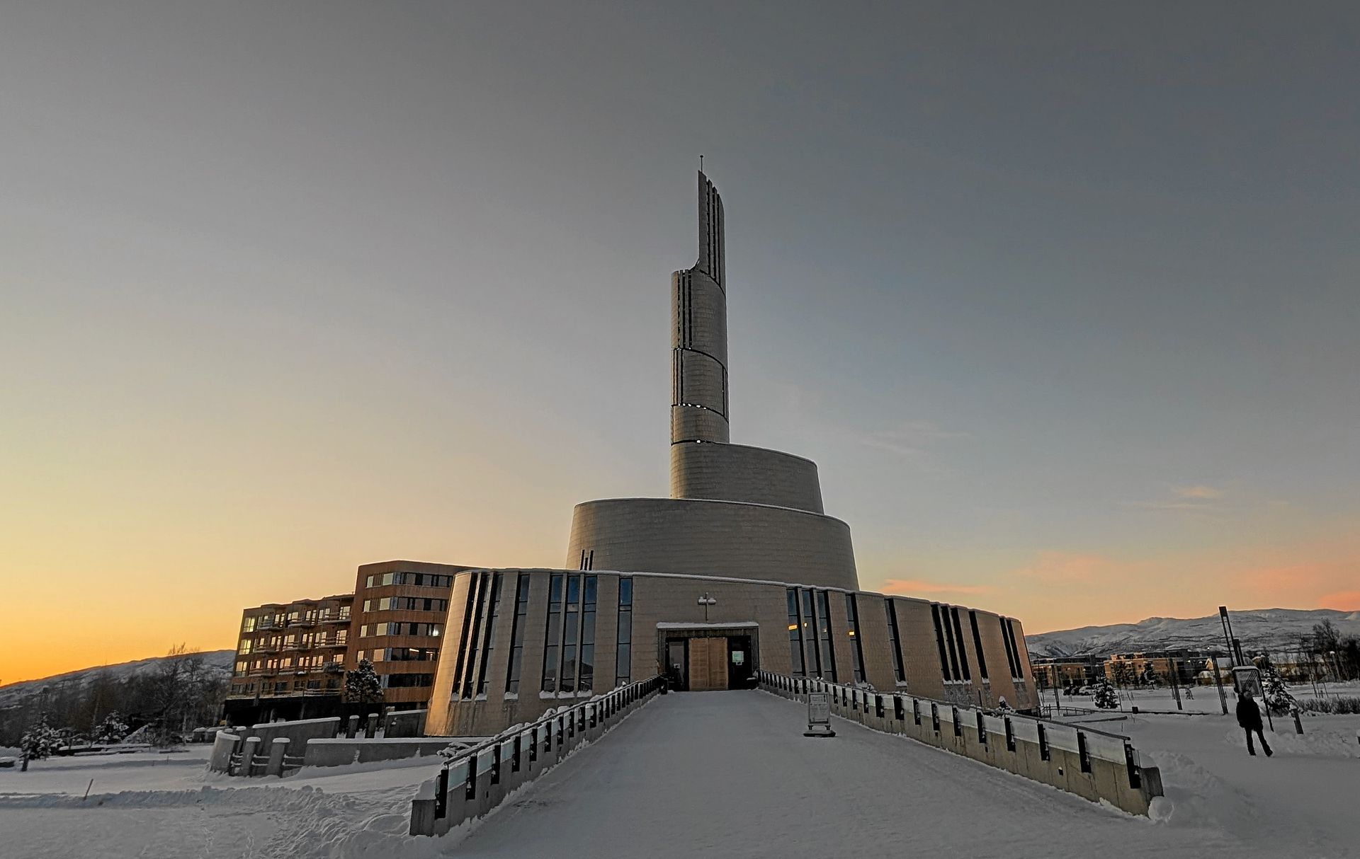 Kirche mit hohem Turmhelm und rundem Sockel, schneebedeckt, vor winterlichem Himmel.