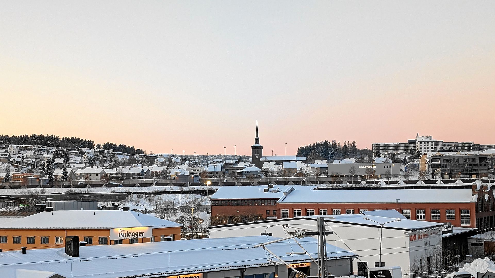 Schneebedeckte Stadtkulisse in der Abenddämmerung mit Kirchturm; im Vordergrund rote Backsteingebäude.