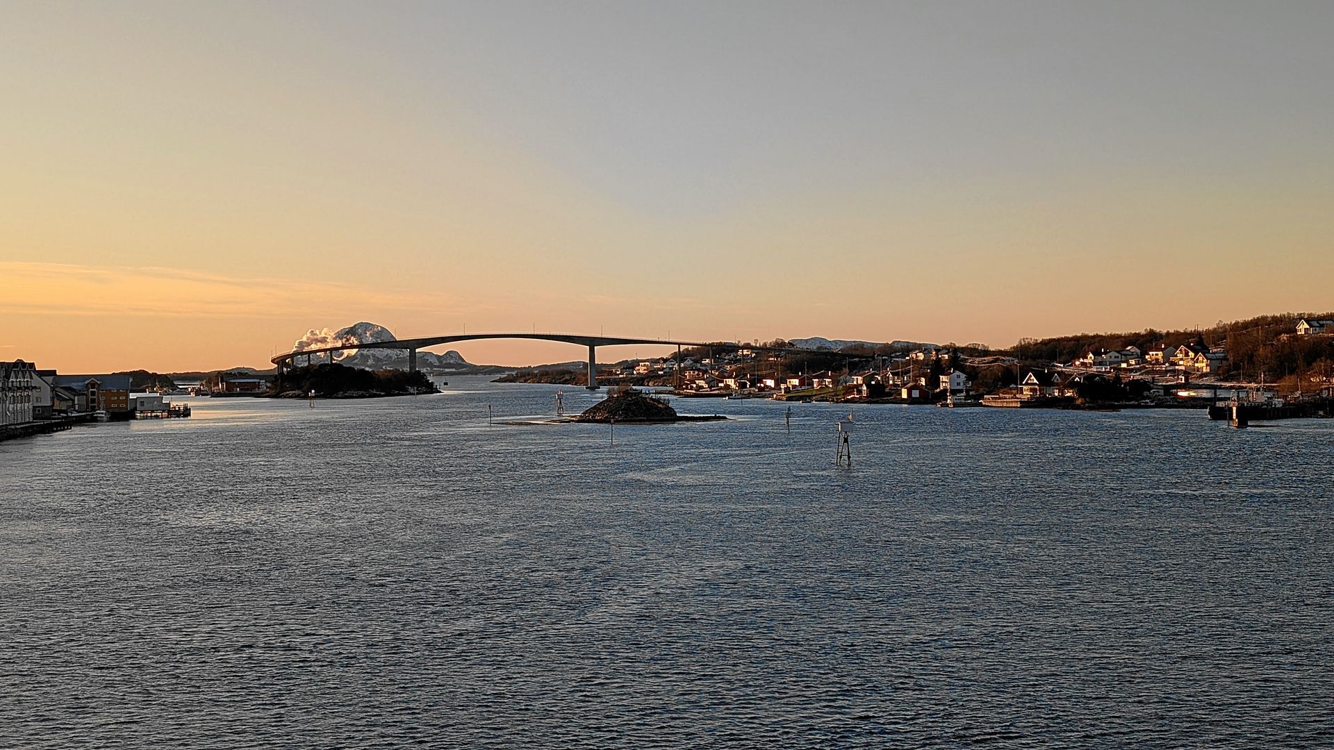 Brücke über Wasser bei Sonnenuntergang; Stadt im Hintergrund.