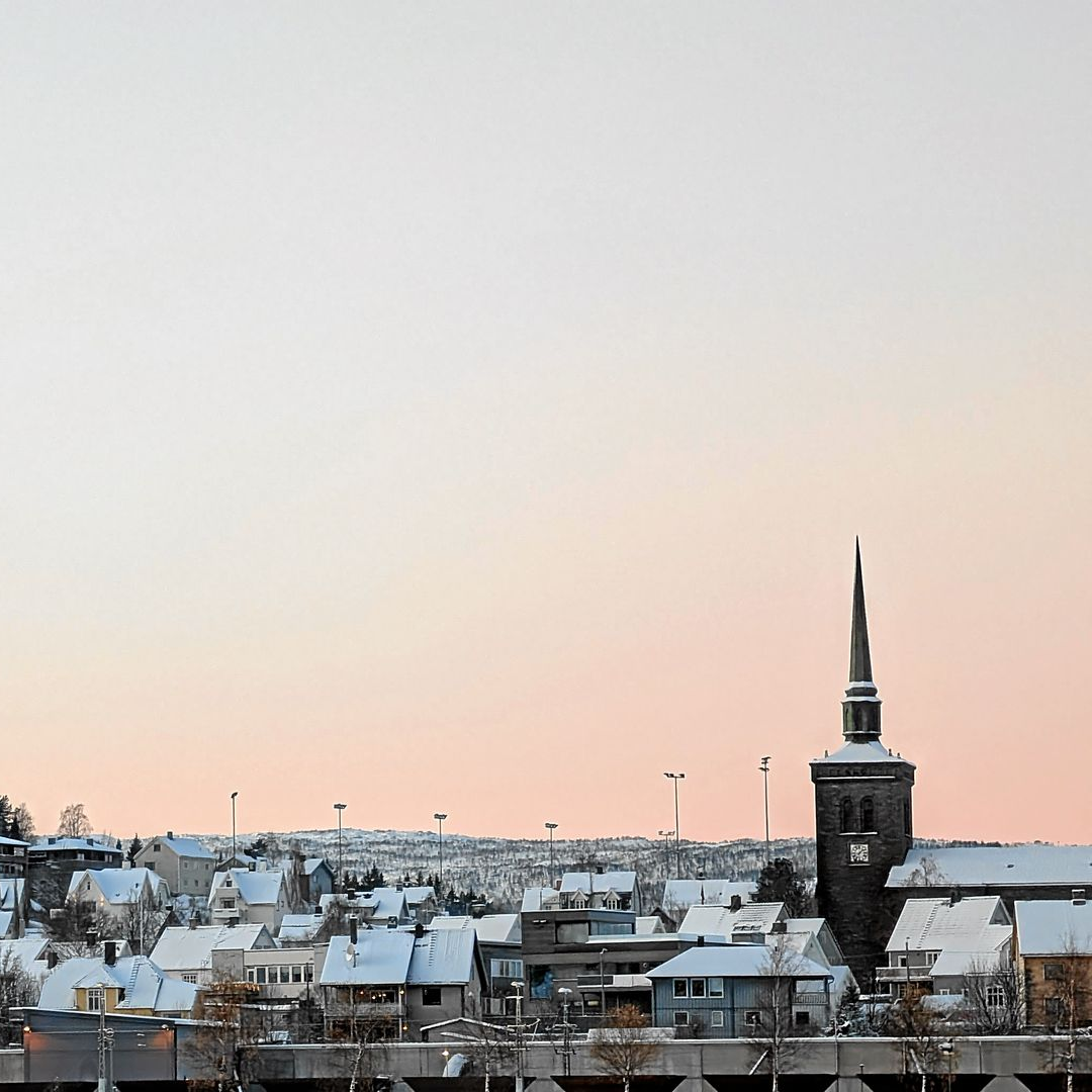 Verschneite Stadtlandschaft mit Kirchturm vor rosa-weißem Himmel.