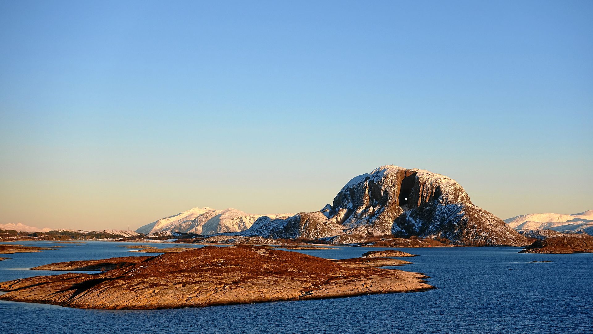 Schneebedeckte Berge und Inseln prägen die blaue Wasserlandschaft unter klarem Himmel.