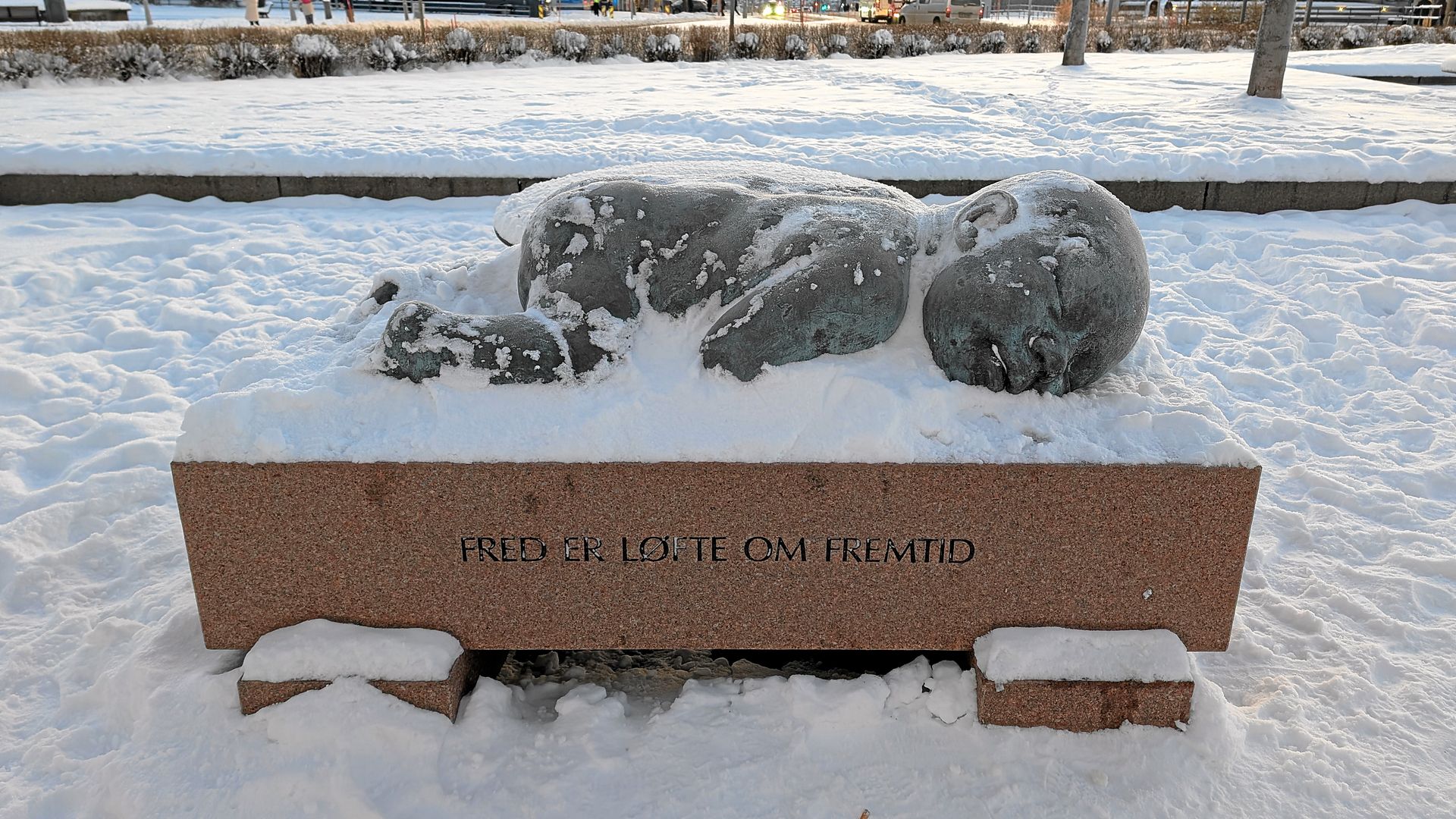 Statue einer schneebedeckten Robbe auf einem Steinsockel mit der Inschrift „MED BÄSTA KAMRATER“ in verschneiter Außenlandschaft.