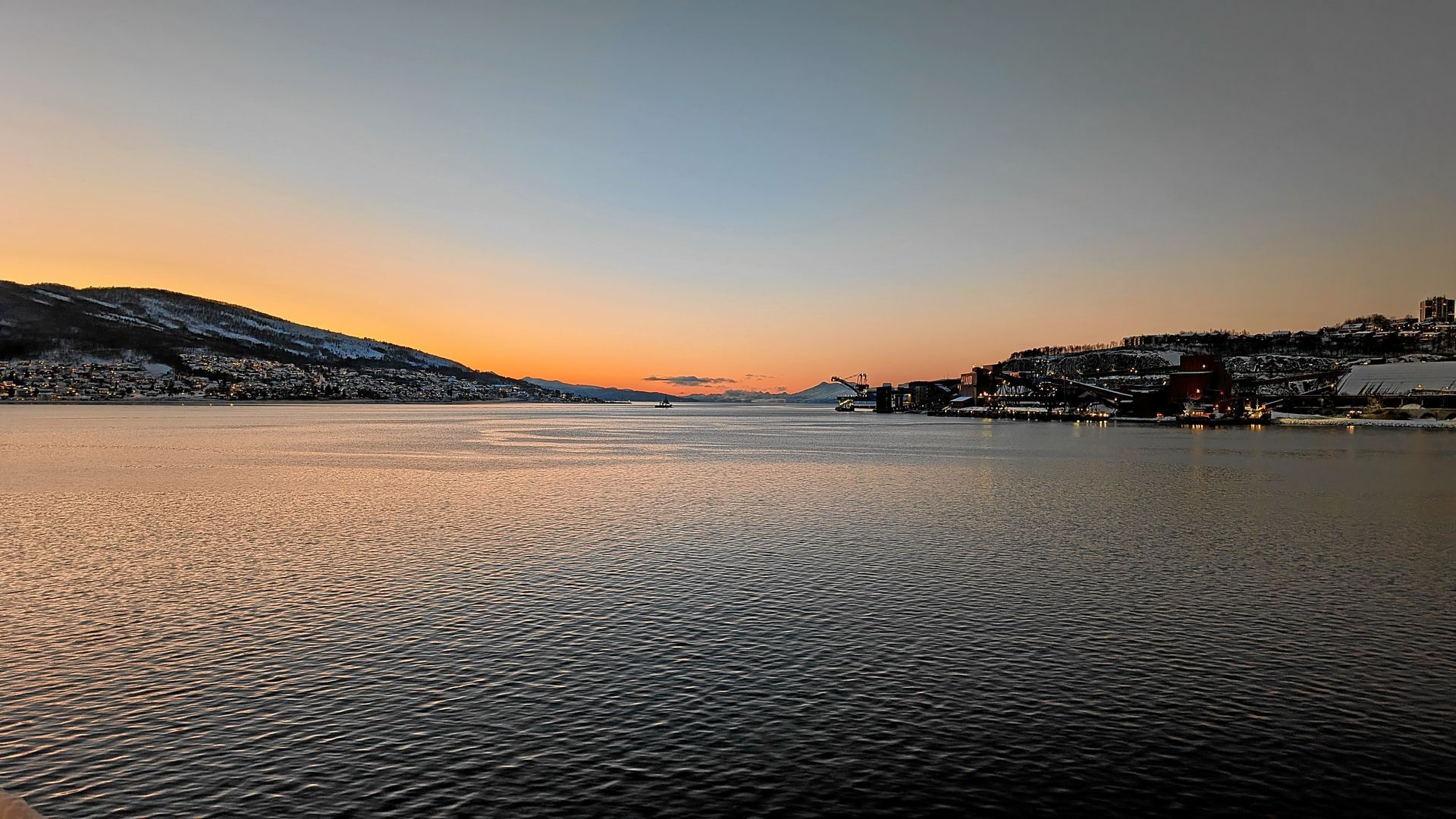Verschneite Landschaft, in der sich ein orange-blauer Sonnenuntergang im Wasser spiegelt.