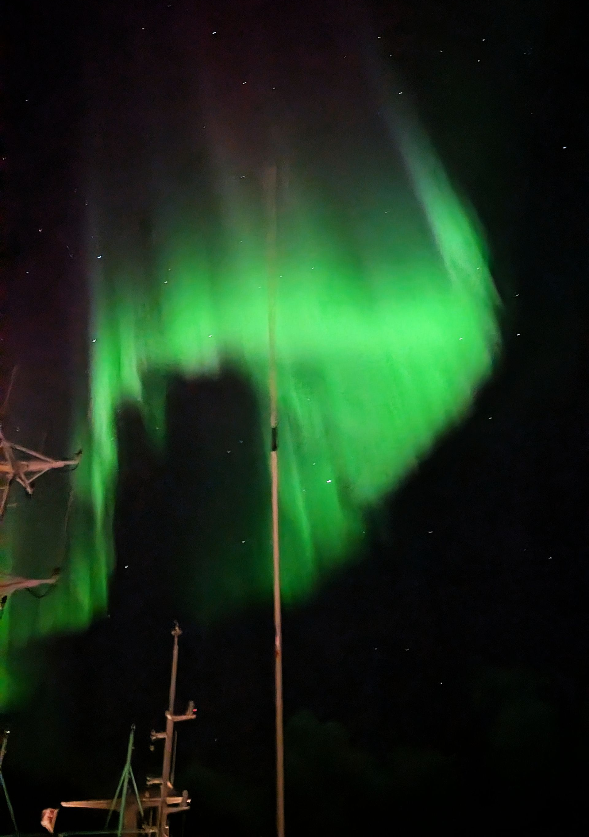 Grüne Nordlichter erleuchten den Nachthimmel über einem dunklen Schiff.