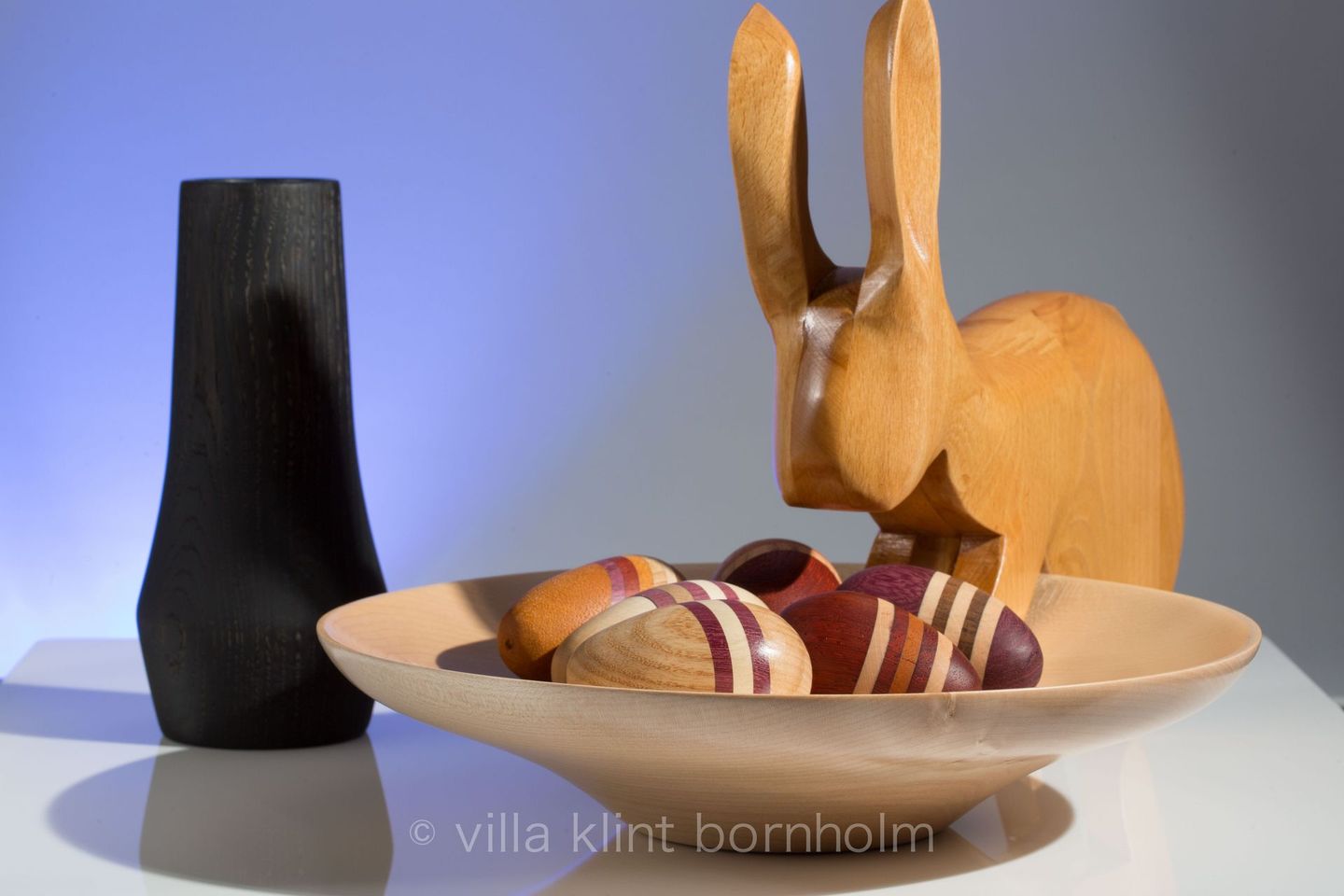 Osterbild: ein Osterhase betrachtet eine Schale mit mehrfarbig gestreiften Ostereiern