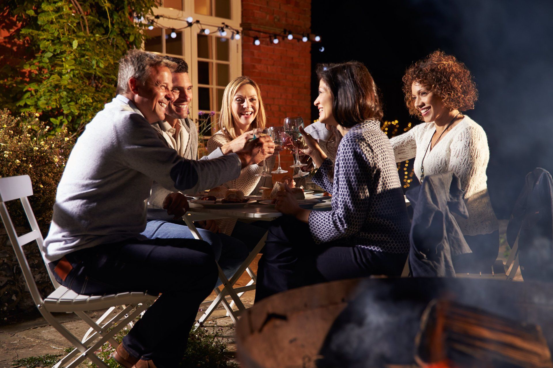 Groupe d'amis  appréciant le repas du soir en plein air autour d'un barbecue