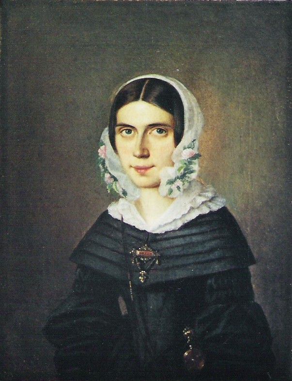 Porträt einer Frau mit weißem Kopftuch, schwarzem Kleid und verzierter Brosche.