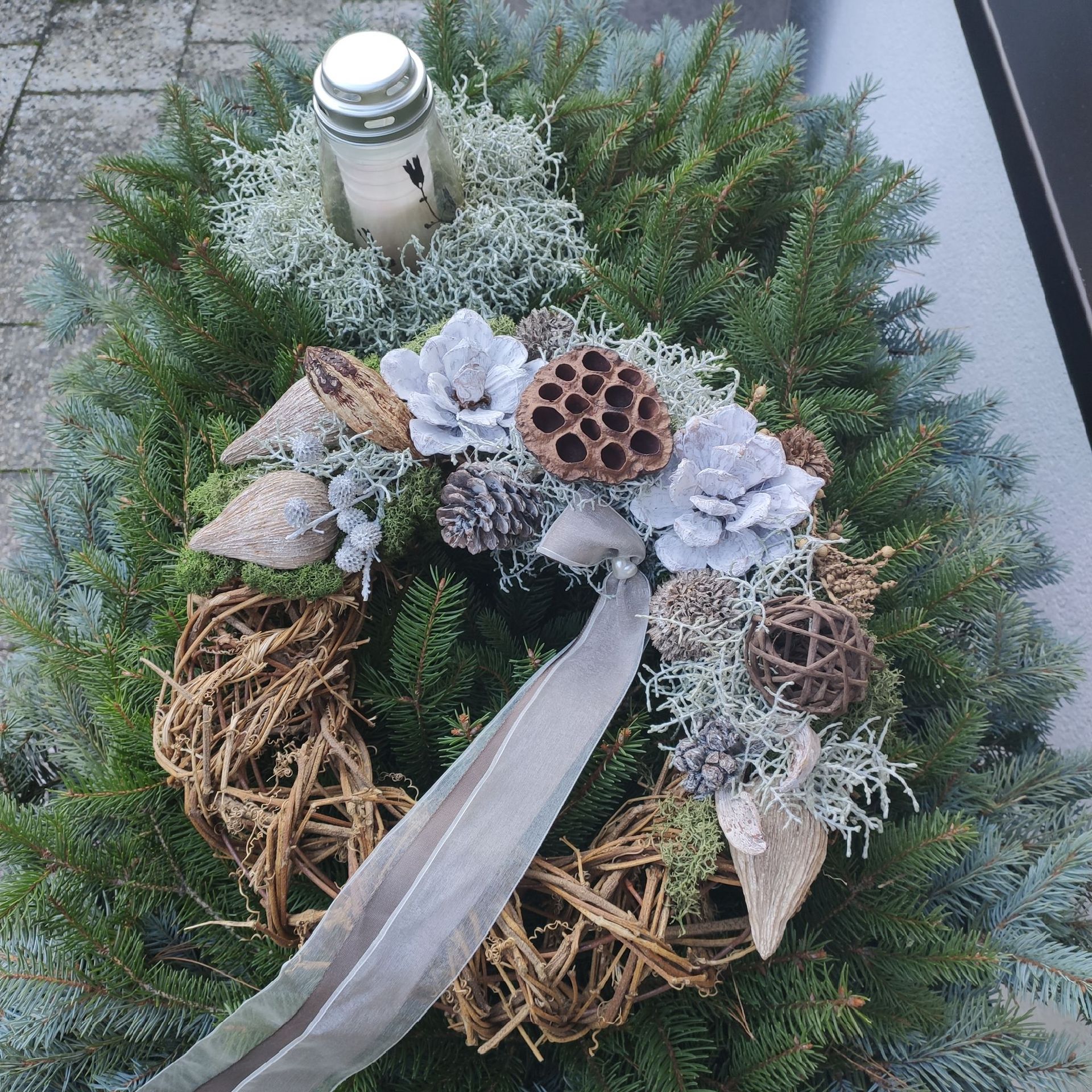 Winterkranz mit Kiefernzweigen, bereiftem Grün, weißen Blüten und einem silbernen Band auf einer Steinoberfläche